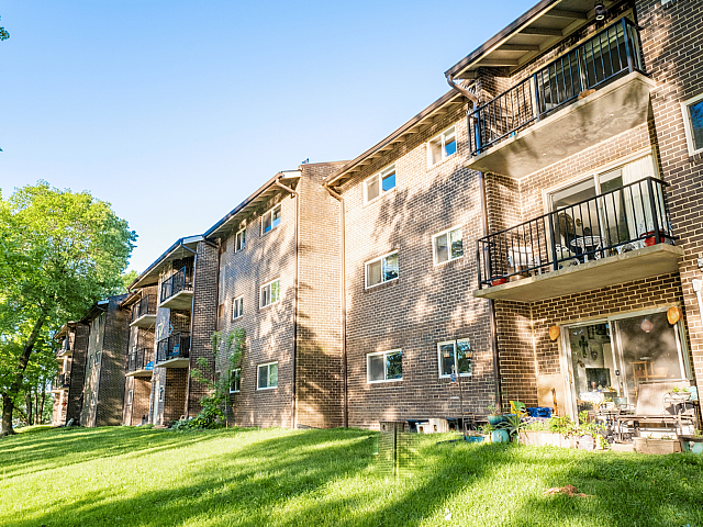 Charming brick apartment building with private balconies and lush green surroundings, offering a peaceful and inviting atmosphere.