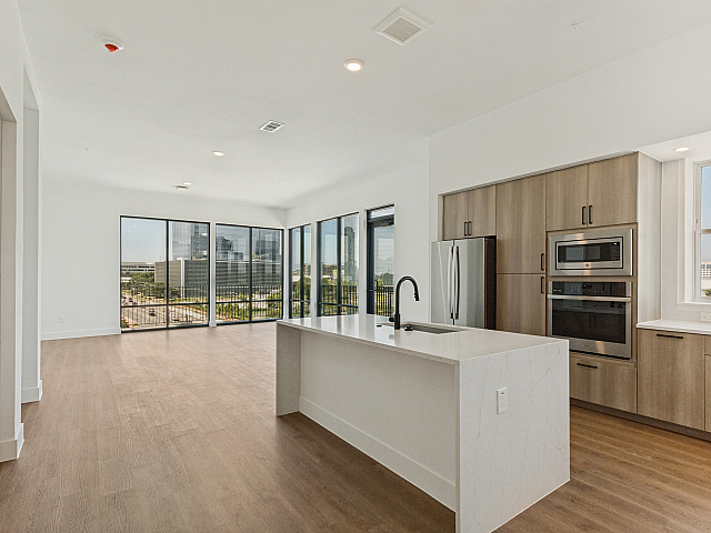 Contemporary open-concept kitchen and living area featuring elegant wood flooring, large windows with stunning city views, and modern stainless steel appliances.