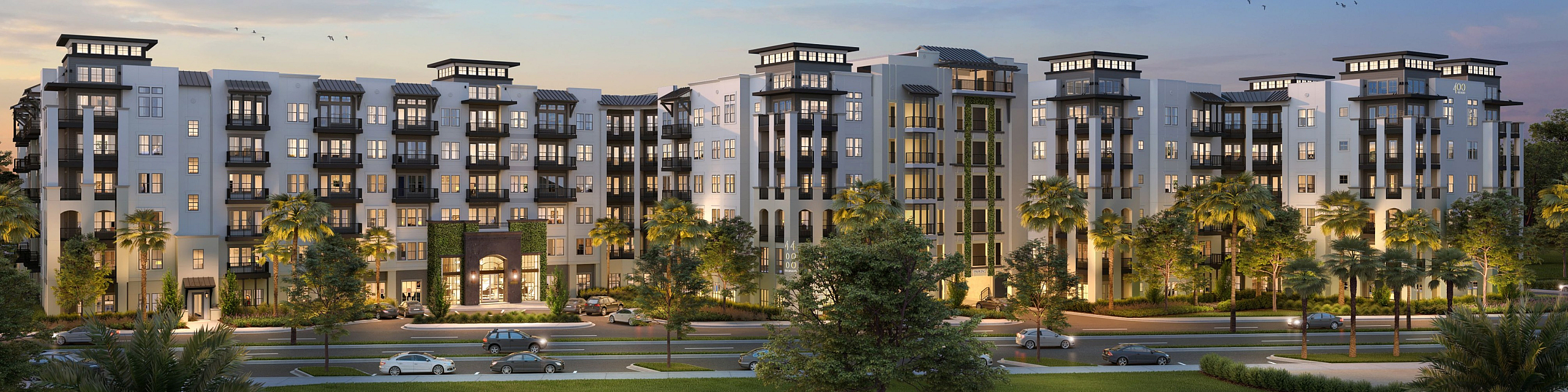 Elegant apartment complex at dusk with palm-lined entrance and modern architecture, showcasing vibrant windows and lush greenery.
