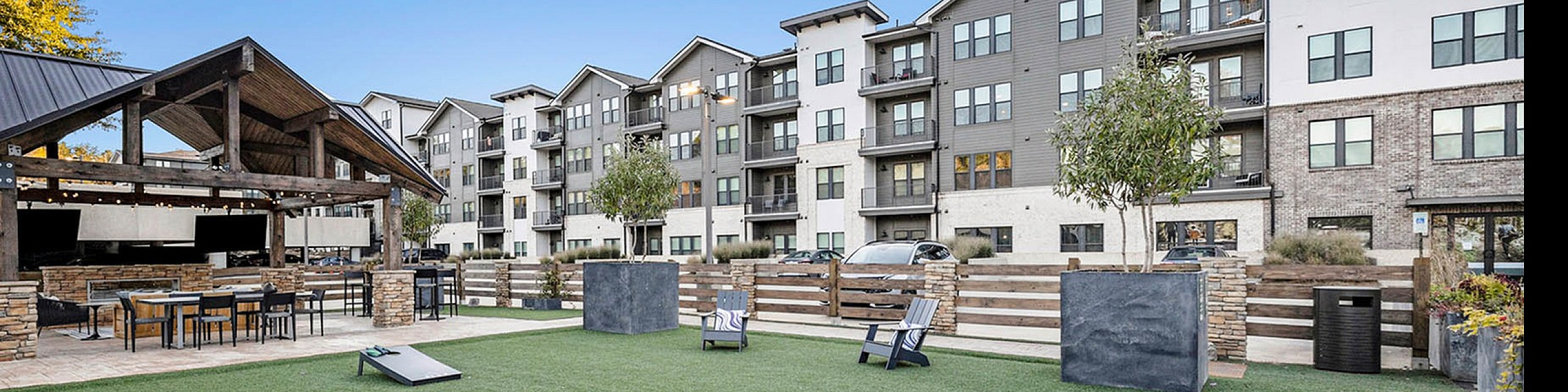 Modern apartment complex with an inviting outdoor area featuring lush green spaces, stylish seating, and a chic gazebo for leisure and entertainment.