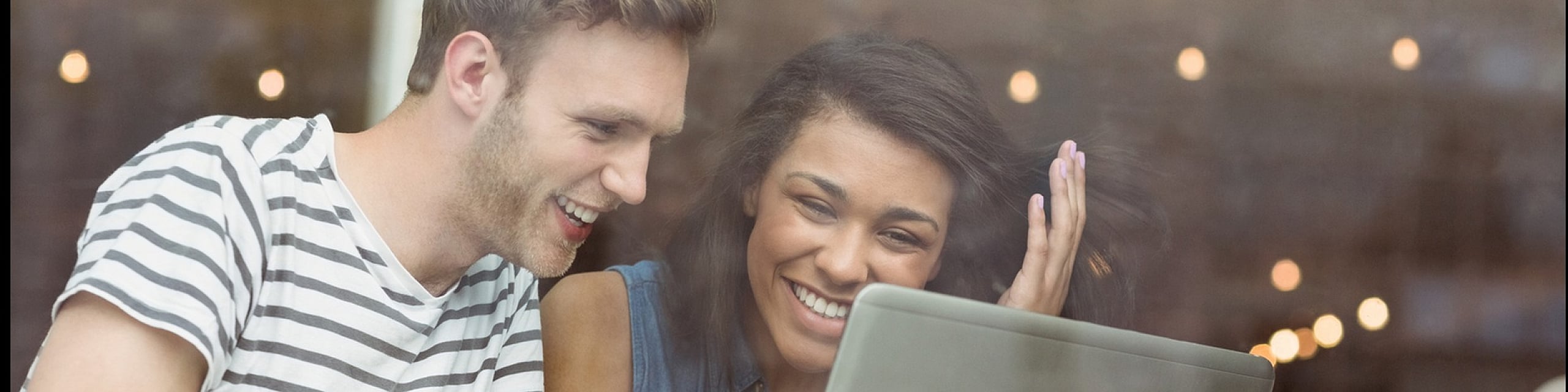 Joyful couple enjoying coffee while browsing on a laptop at a cozy cafe, showcasing a friendly atmosphere.