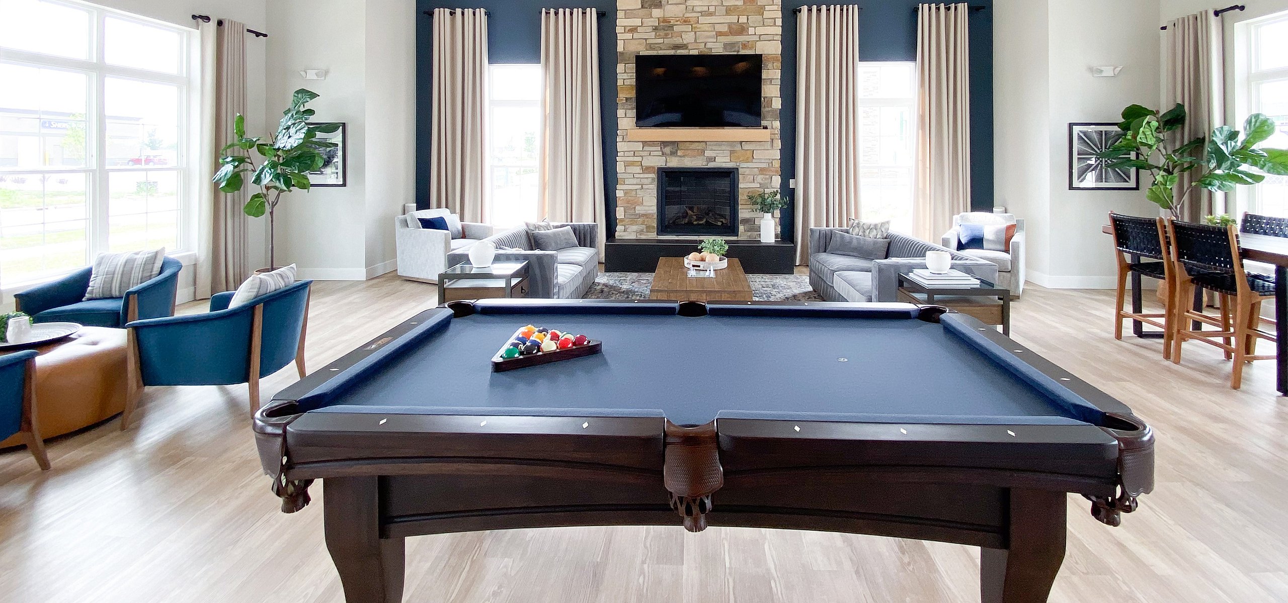 Luxurious open-concept living space with a stylish pool table, elegant stone fireplace, and modern seating area, perfect for entertaining.