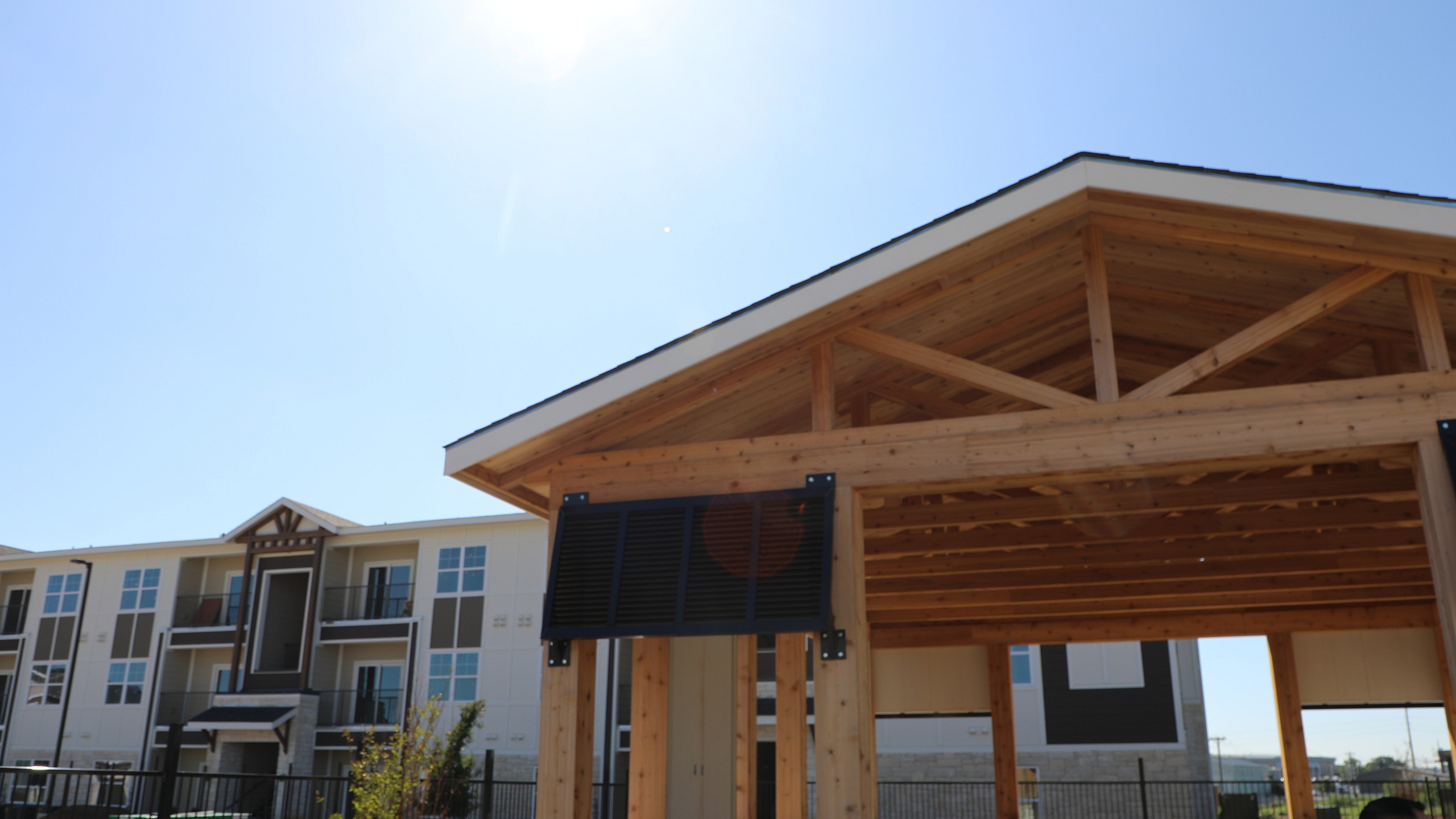 Modern apartment complex with a stylish wooden pavilion under a clear blue sky, offering a blend of contemporary architecture and outdoor leisure space.