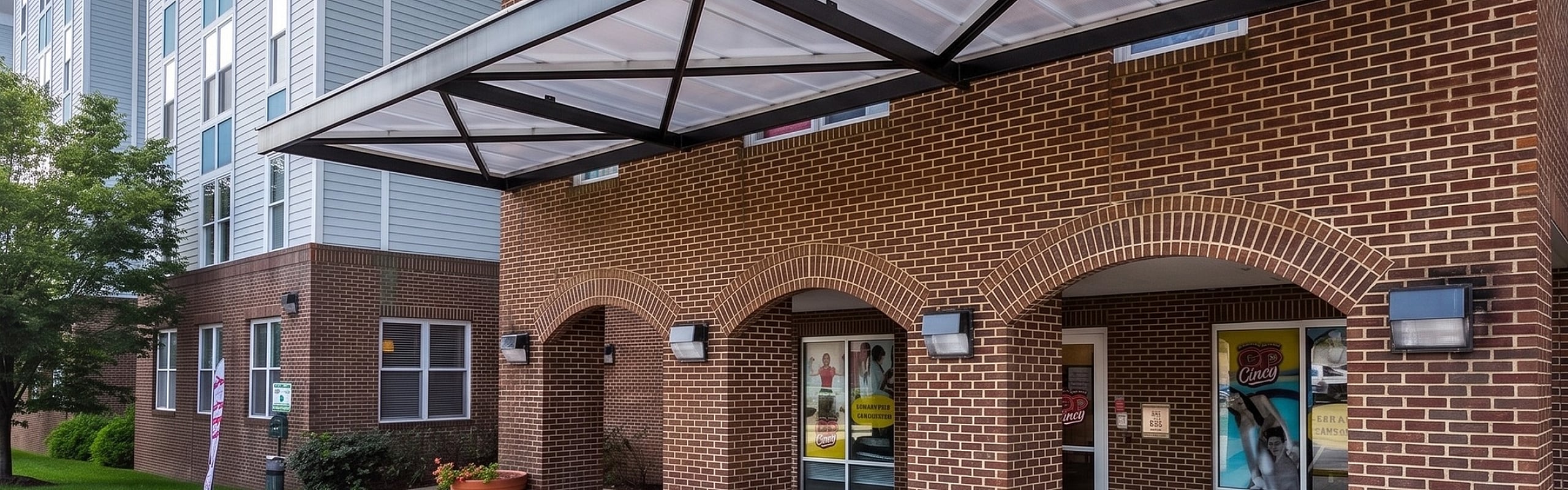 Modern apartment entrance featuring elegant brickwork and a stylish metal canopy, complemented by vibrant potted plants.