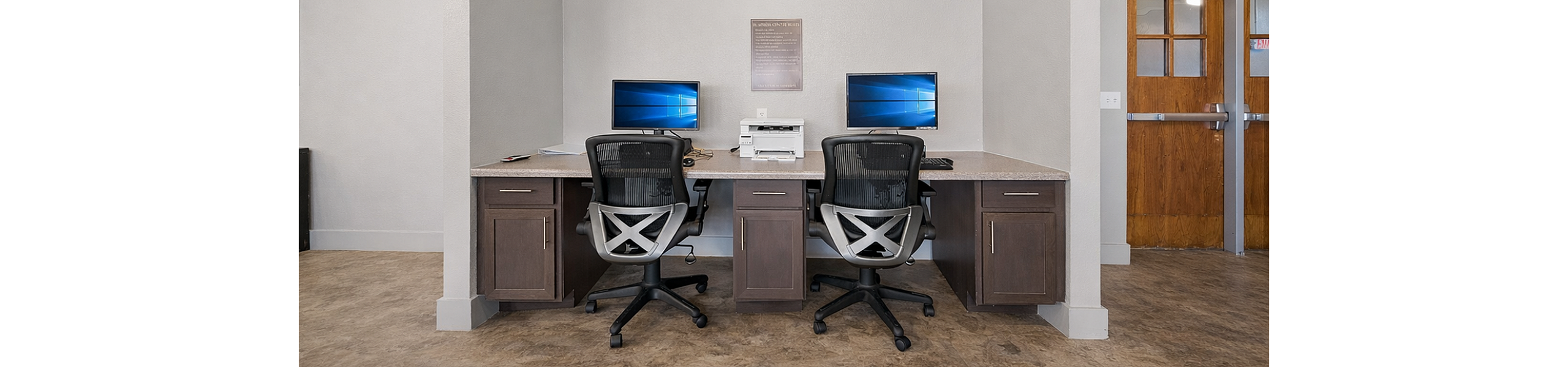 Modern communal workspace with two ergonomic chairs, dual monitors, and ample desk space beneath efficient air conditioning.