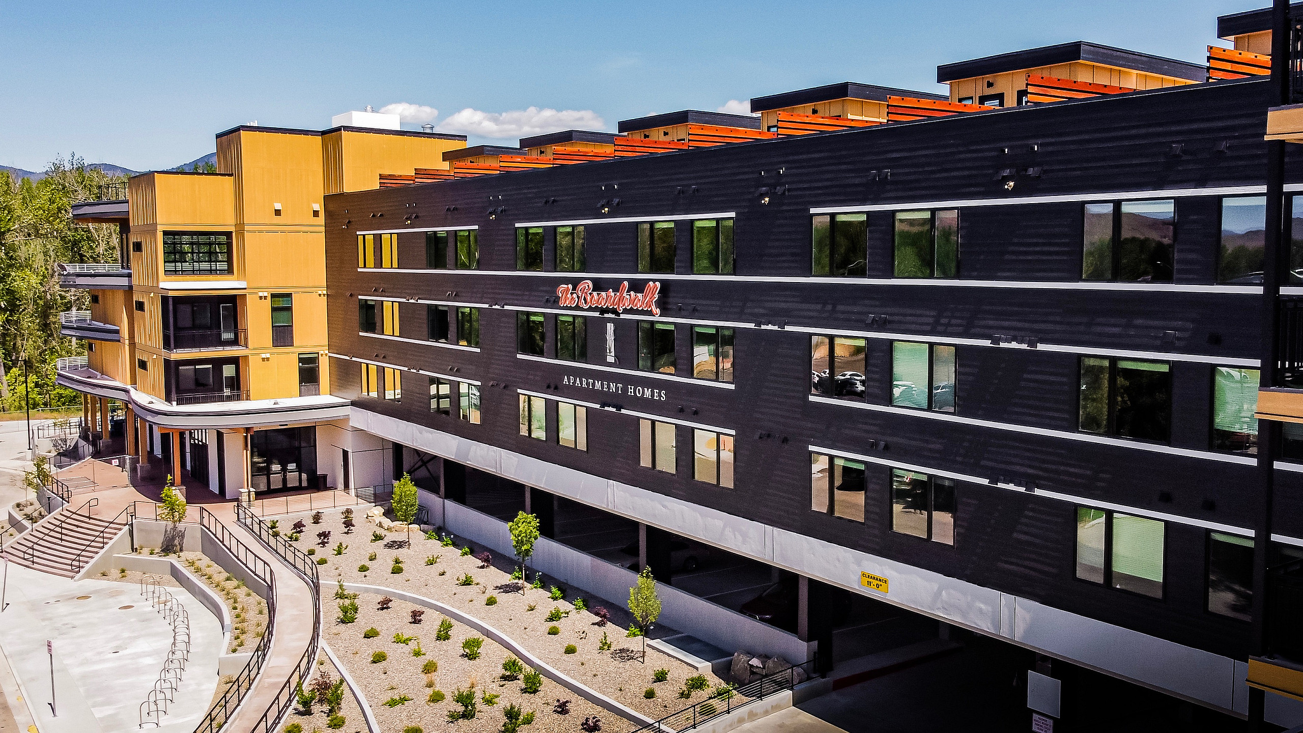 Modern apartment complex featuring sleek architecture, large windows, and landscaped pathways, surrounded by scenic views and vibrant greenery.