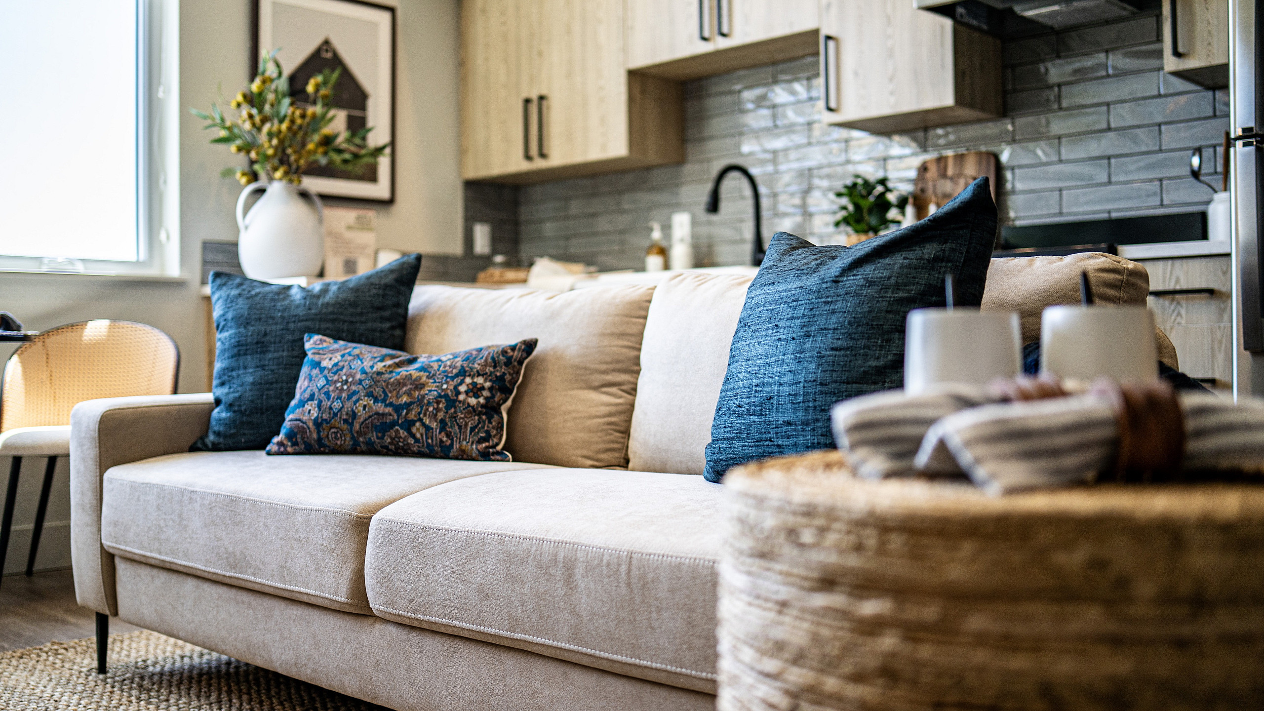 Chic living area with a cozy beige sofa, stylish throw pillows, and modern kitchen backdrop.