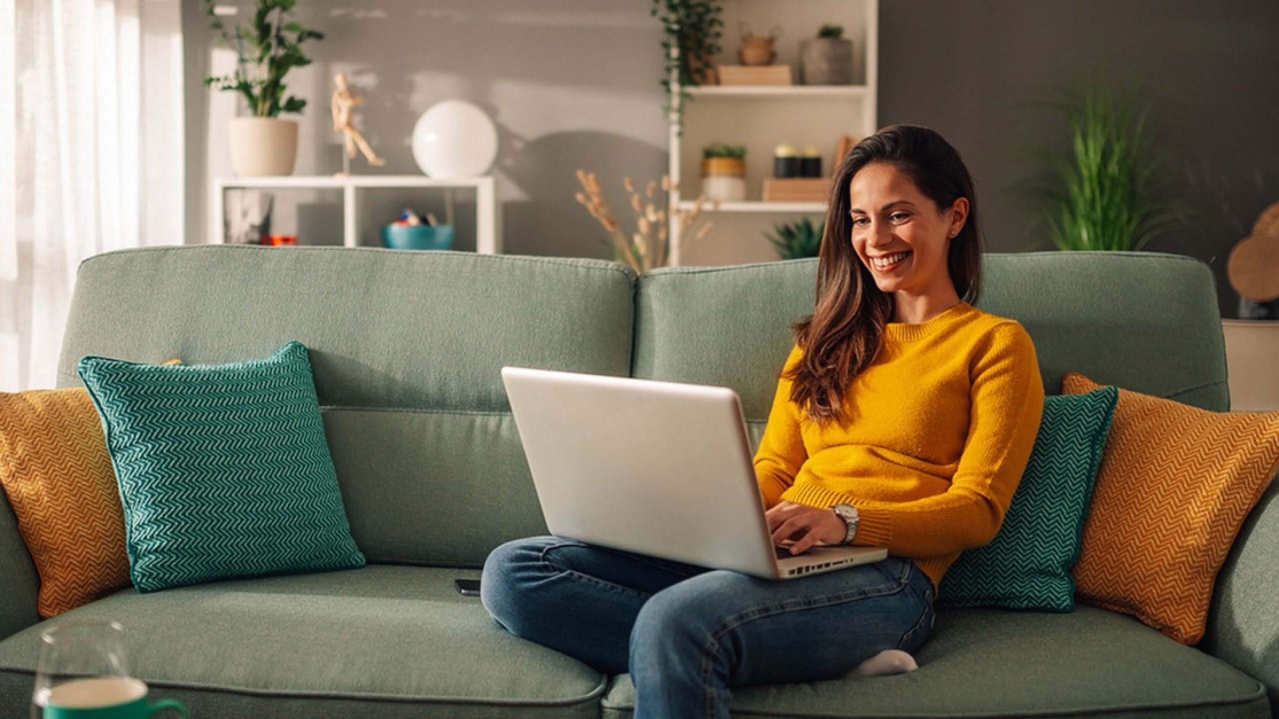 Cozy living room with a cheerful ambiance featuring a woman working on a laptop, surrounded by colorful cushions and vibrant green plants.