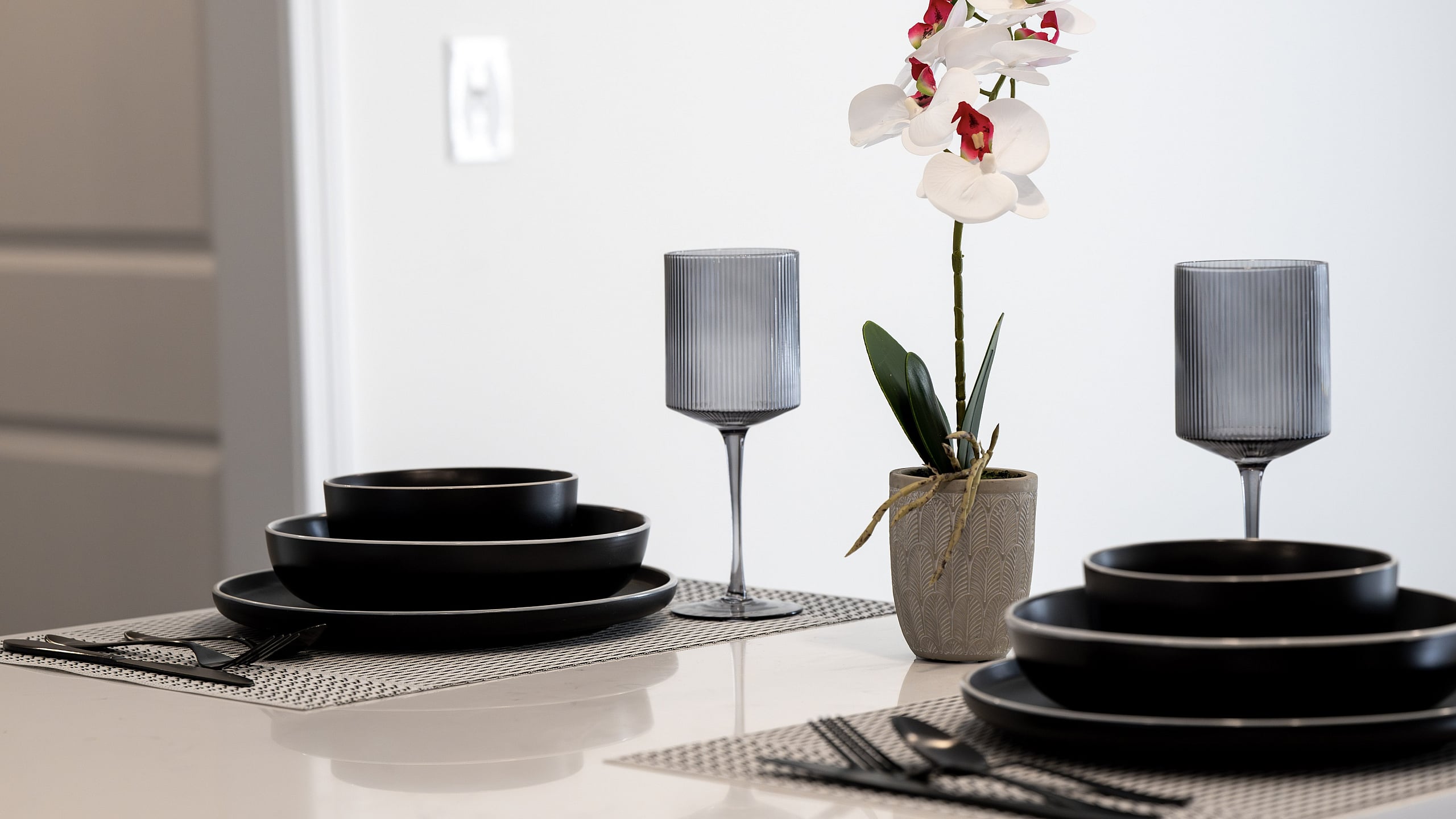 Elegant dining setup with sleek black dishware on a modern table, adorned by a vibrant orchid centerpiece and stylish glassware.