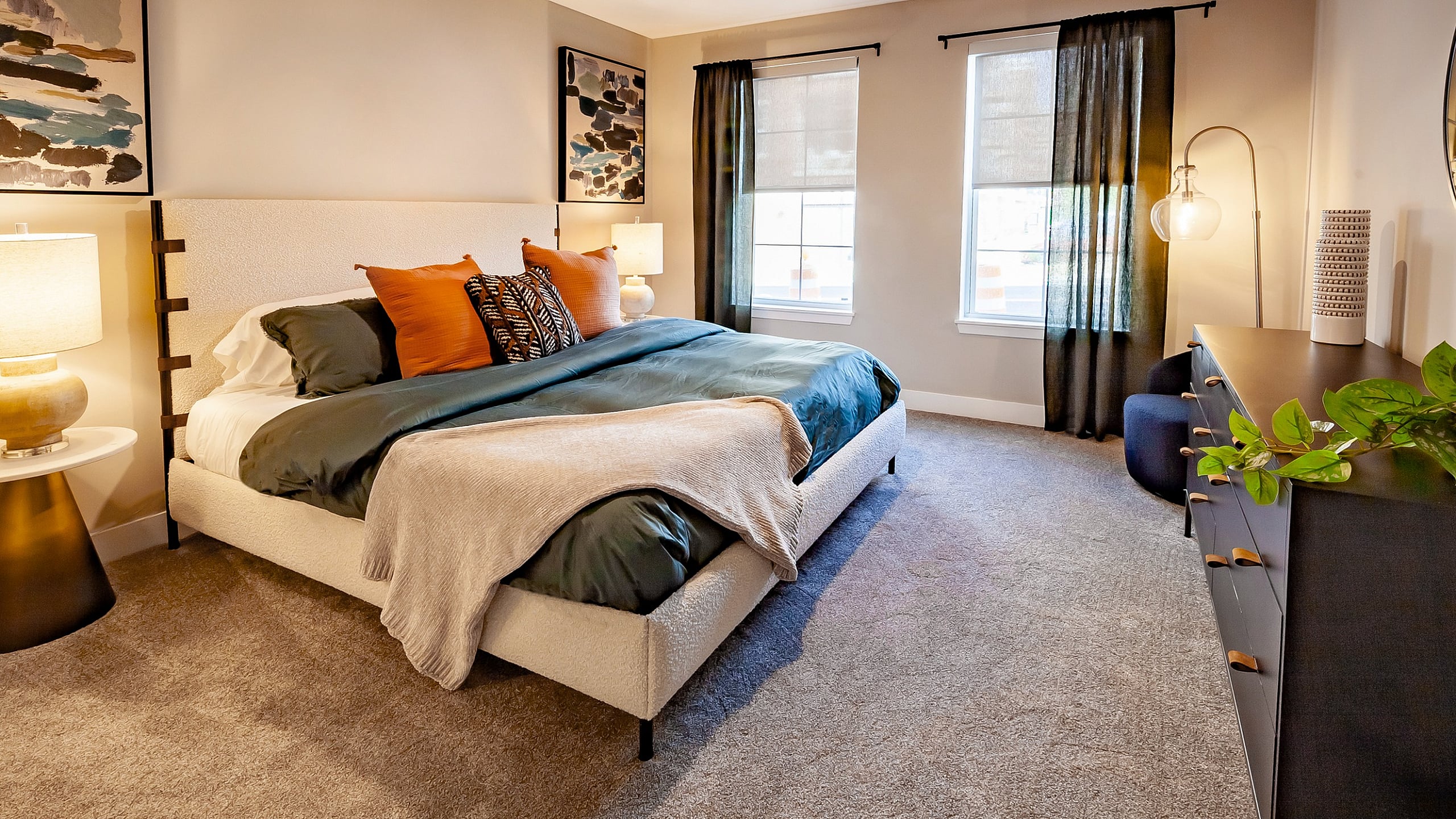 Inviting bedroom with modern decor, featuring a plush bed, stylish bedside lamps, and vibrant artwork, complemented by natural light from large windows.