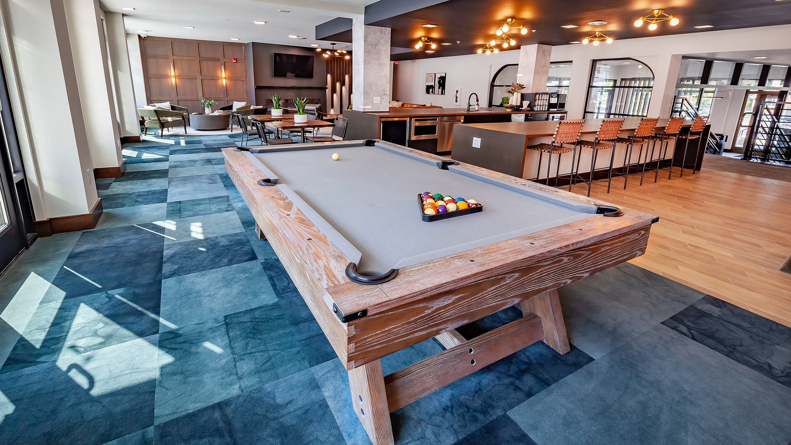 Inviting and modern lounge area featuring a stylish pool table, chic bar seating, and abundant natural light.