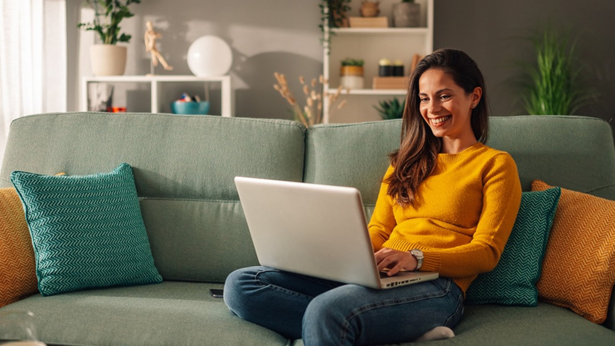 Cozy living room with soft lighting, a comfortable green sofa adorned with colorful cushions, and a person enjoying a laptop, creating a warm and inviting atmosphere.