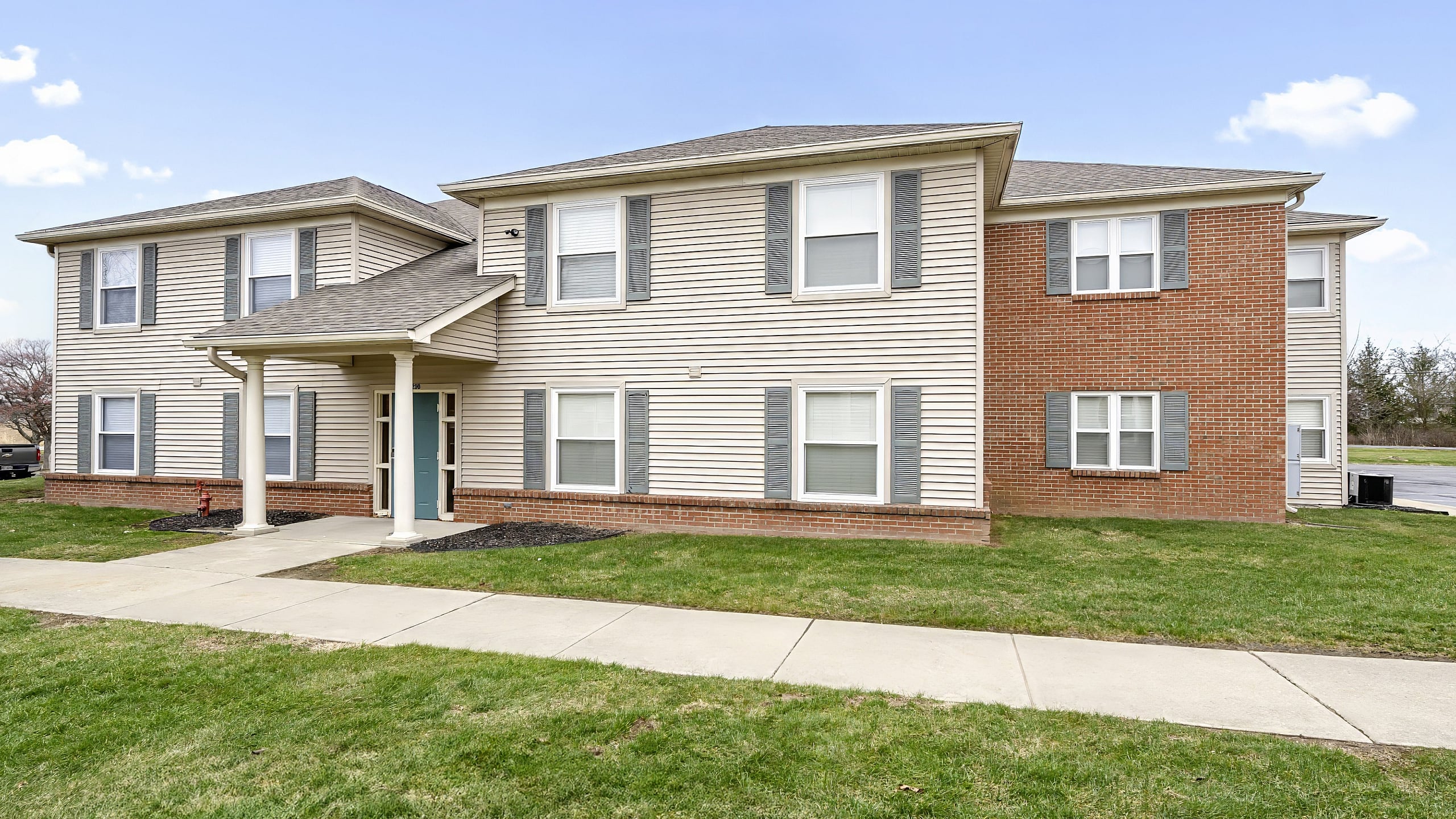 Charming two-story apartment building with brick and siding exterior, surrounded by lush green lawns and spacious walkways.