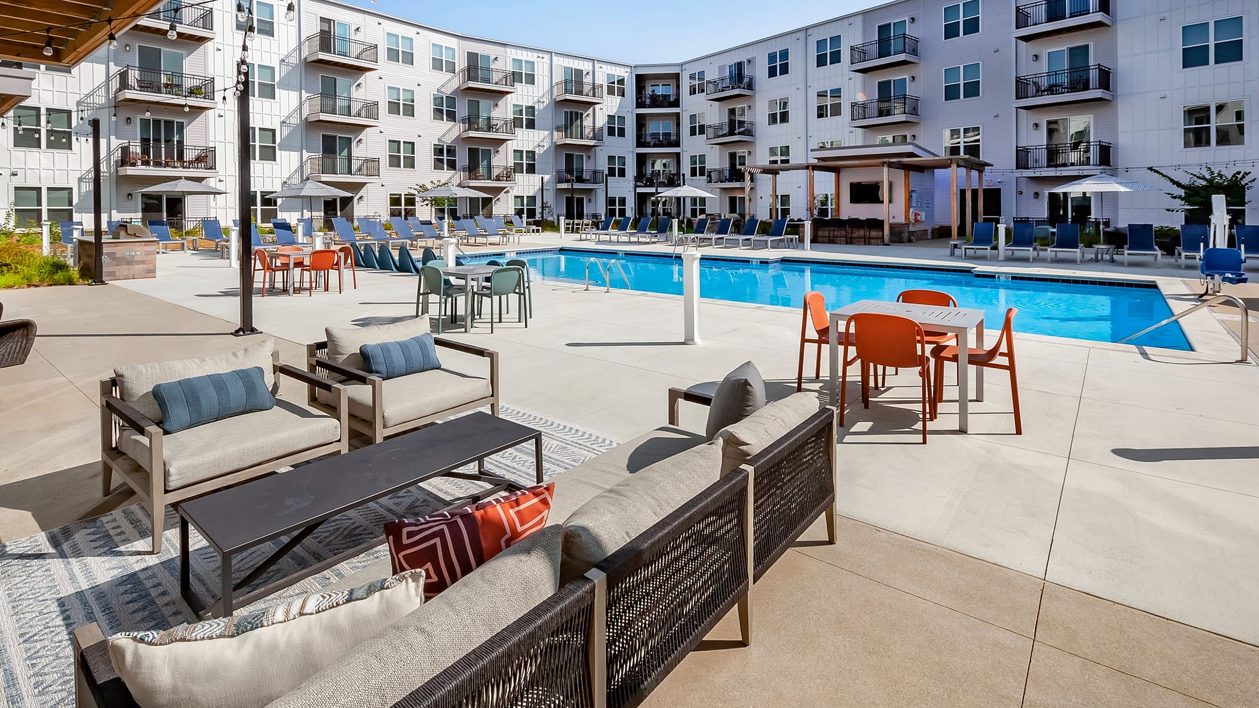 Luxurious apartment complex showcasing a vibrant pool area, spacious outdoor seating, and modern balconies, perfect for relaxation and entertainment.