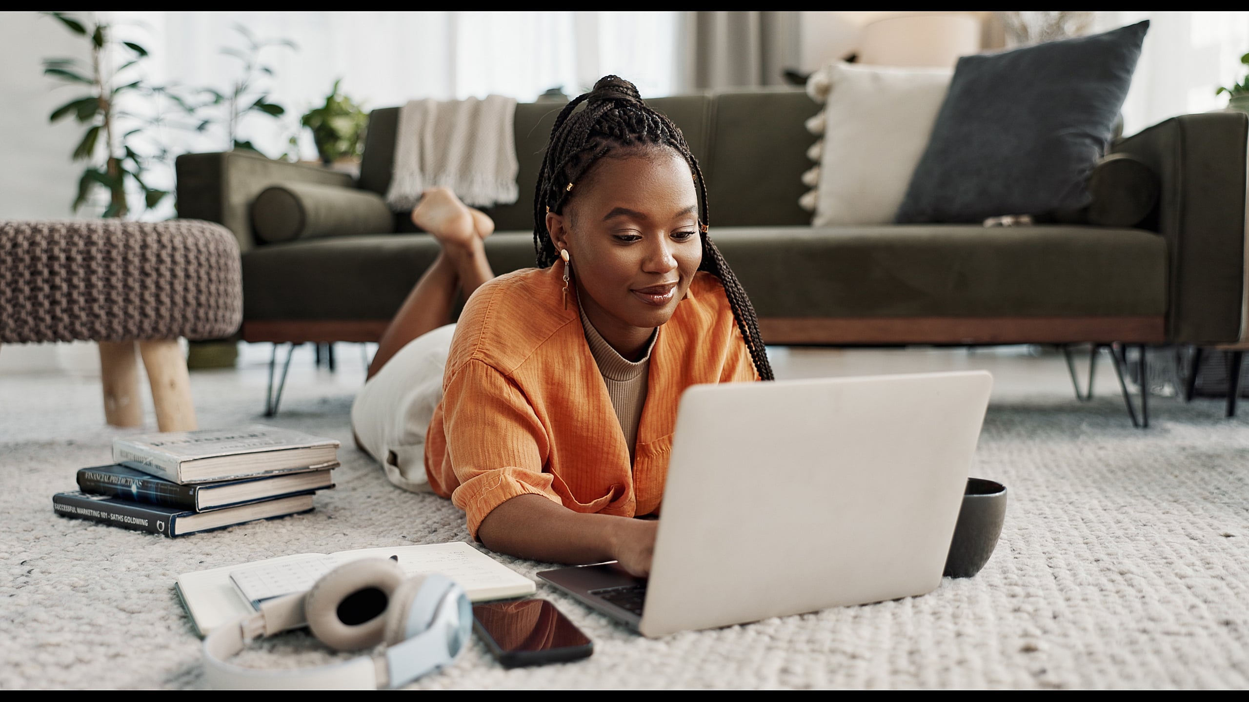 Cozy living space with a person relaxing on a plush carpet, surrounded by a stylish sofa, books, and a laptop, creating a perfect blend of comfort and productivity.