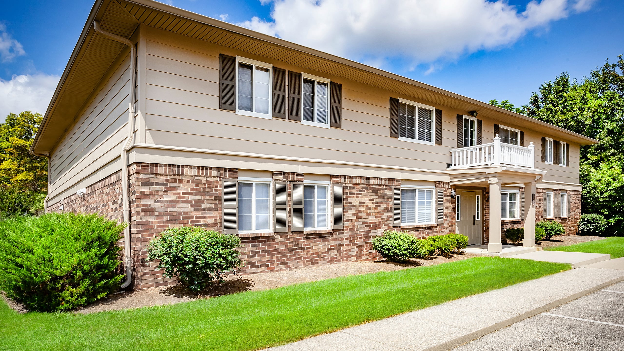 Charming two-story apartment complex with classic brick and siding exterior, surrounded by lush greenery and a bright, inviting atmosphere.