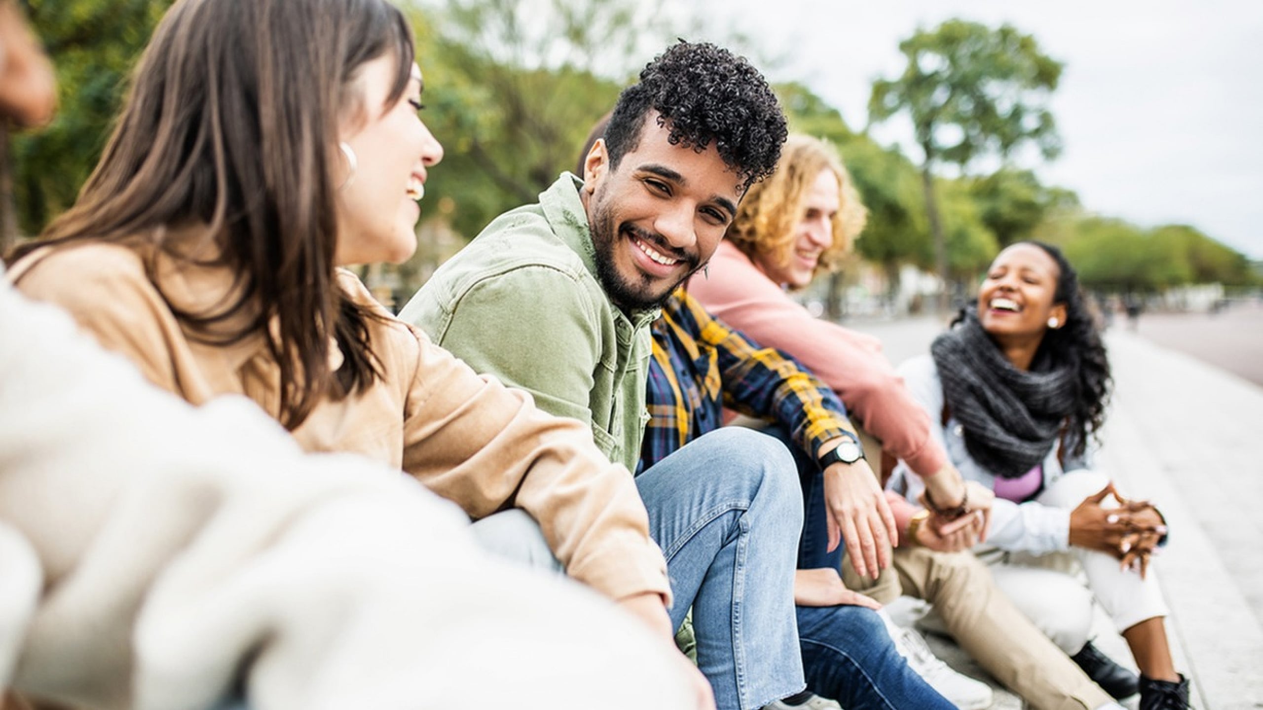 Joyful group of friends sitting outdoors, sharing laughter and positive energy on a sunny day.