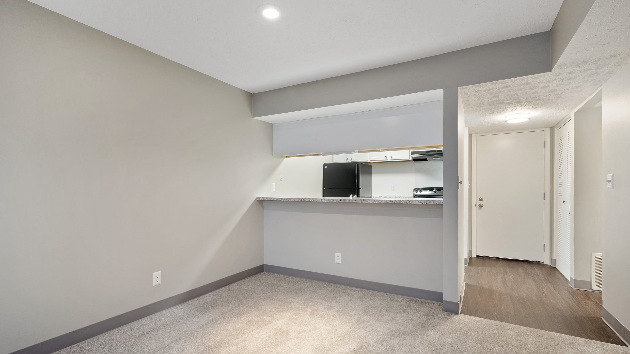 Inviting interior showcasing an open-concept living space with plush carpeting, modern kitchen pass-through, and sleek hardwood entryway.