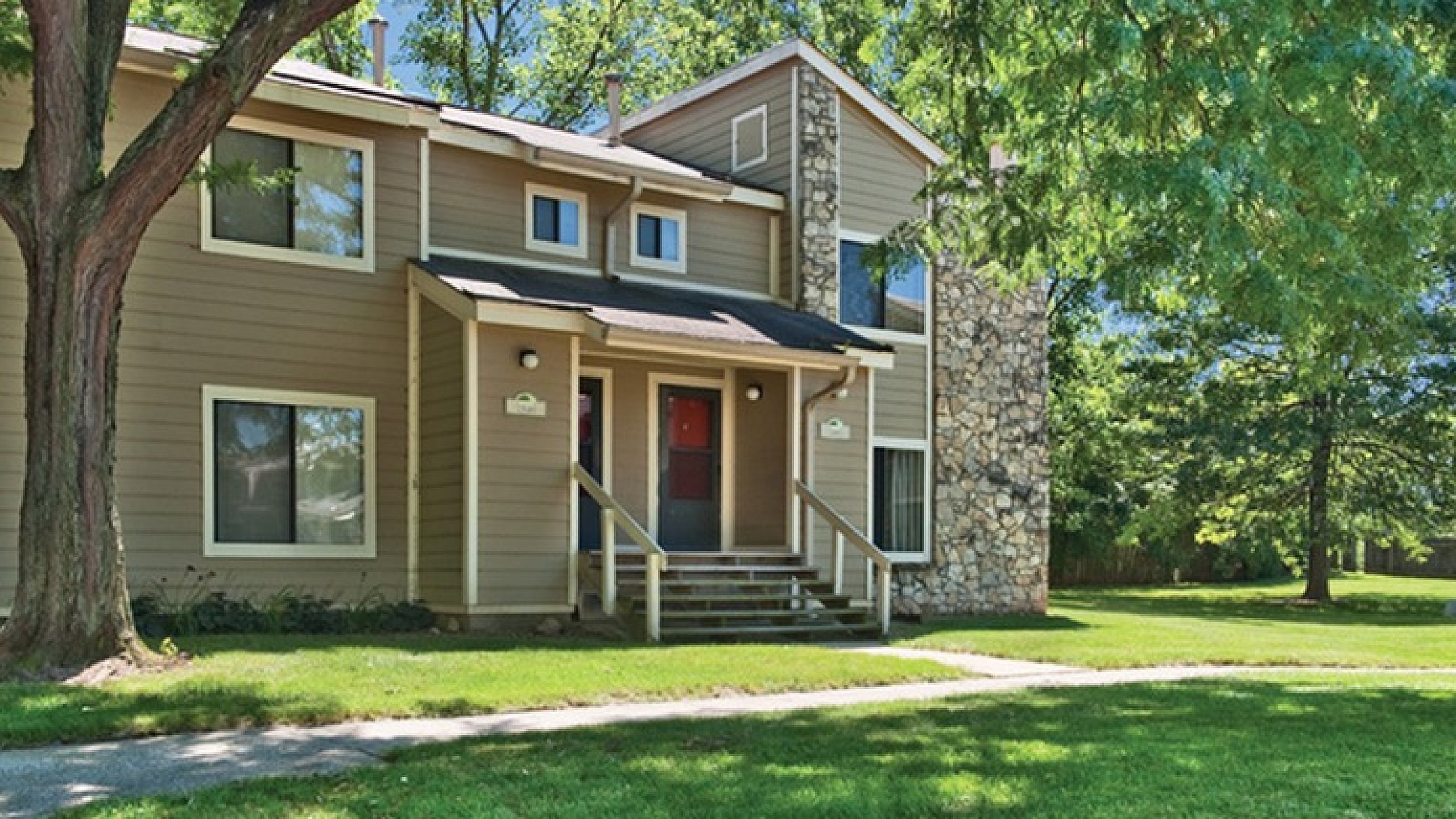 Charming two-story apartment with a stone facade, nestled amidst lush greenery and vibrant trees.