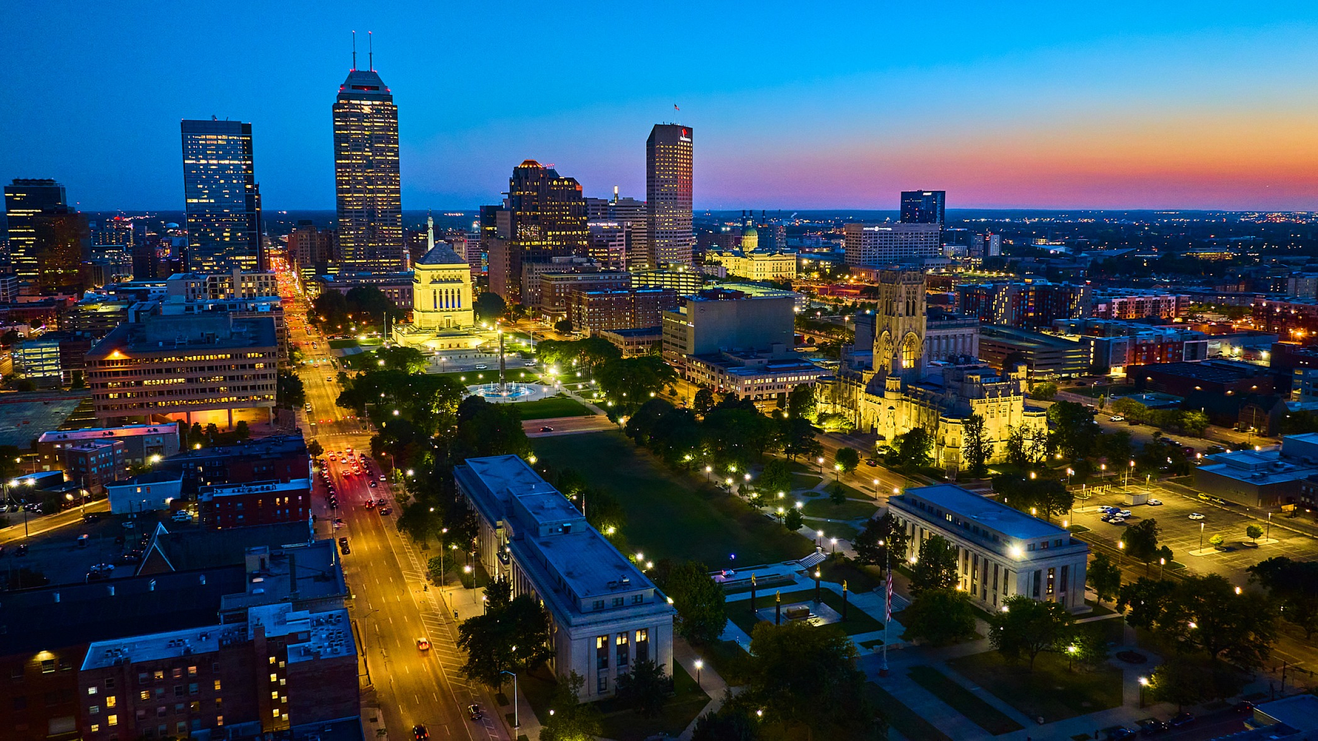 Captivating aerial view of downtown Indianapolis at dusk, with illuminated skyscrapers and a colorful sunset sky.