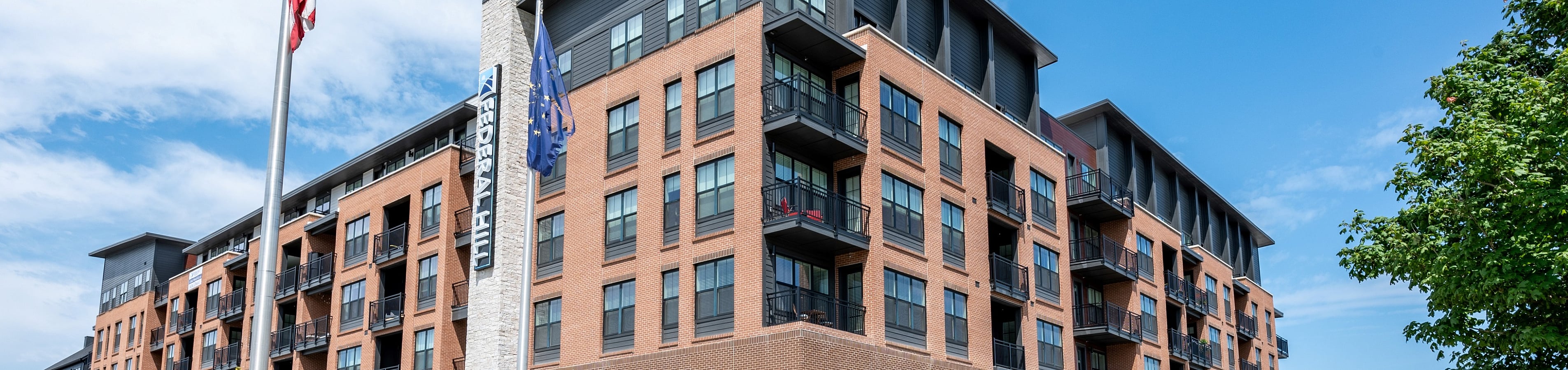 Modern apartment building exterior featuring brick design, large windows, and spacious balconies under a clear blue sky.