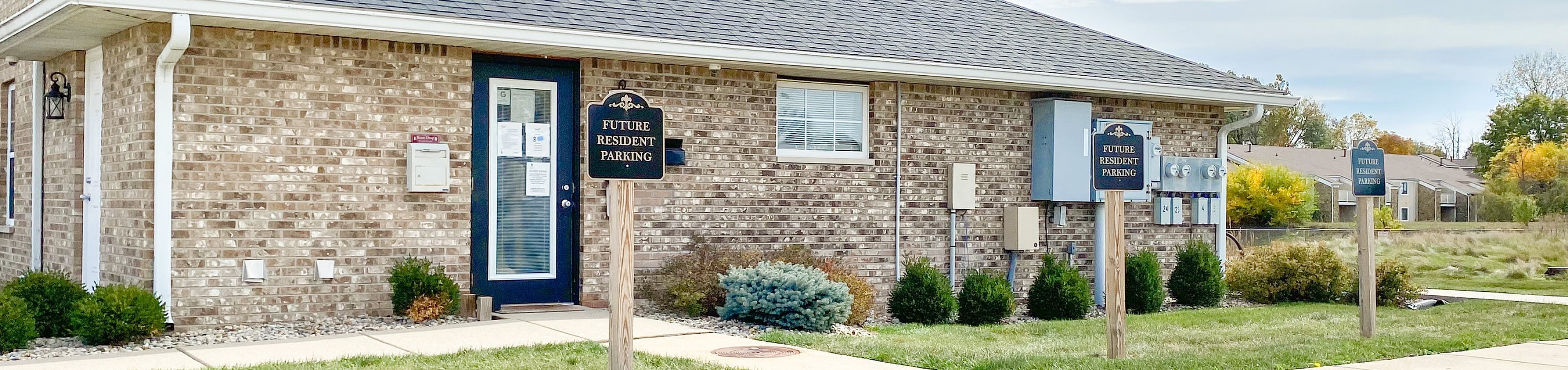 Inviting brick building with future resident parking, surrounded by lush greenery and a serene, open landscape.