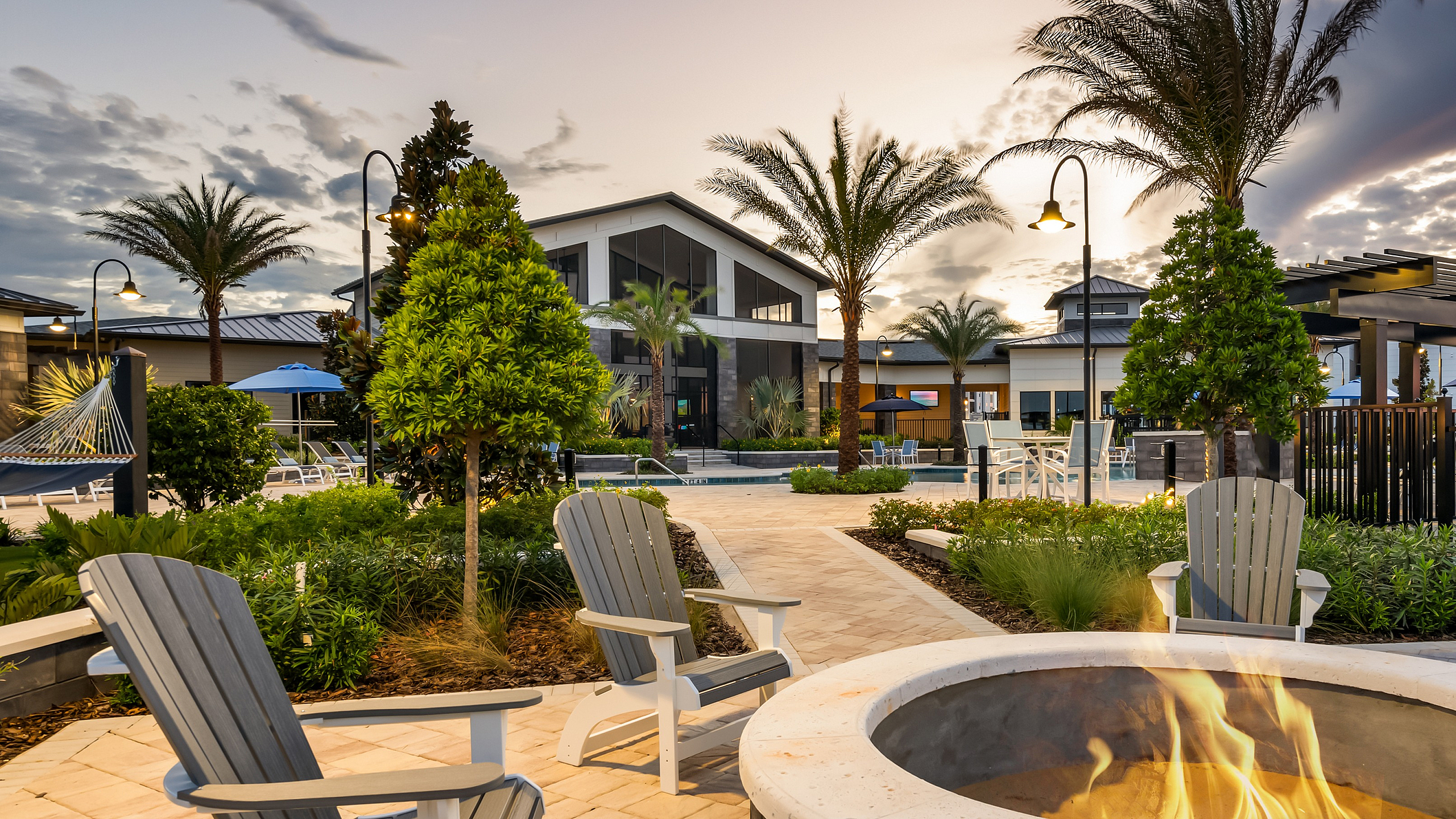 Inviting outdoor lounge area with cozy fire pit, surrounded by lush greenery and palm trees at sunset, perfect for relaxation.