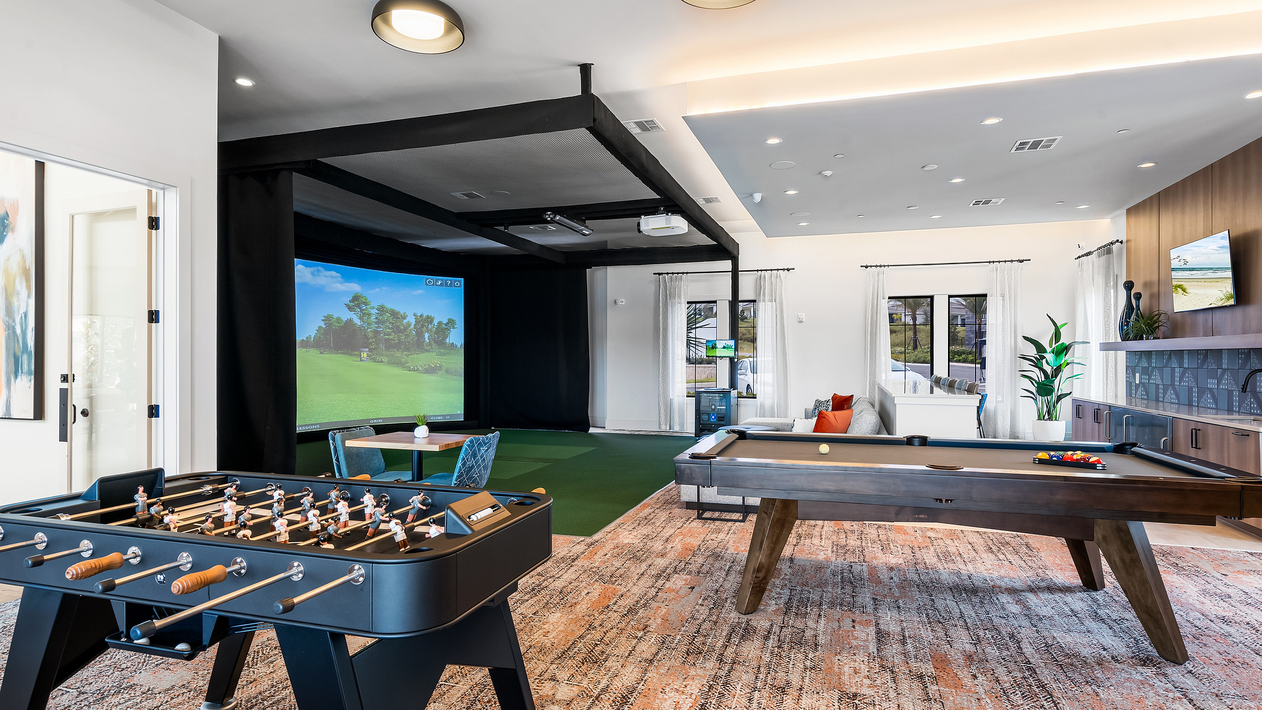 Luxurious entertainment room with a pool table, foosball table, and a golf simulator, accented by modern decor and plush seating.