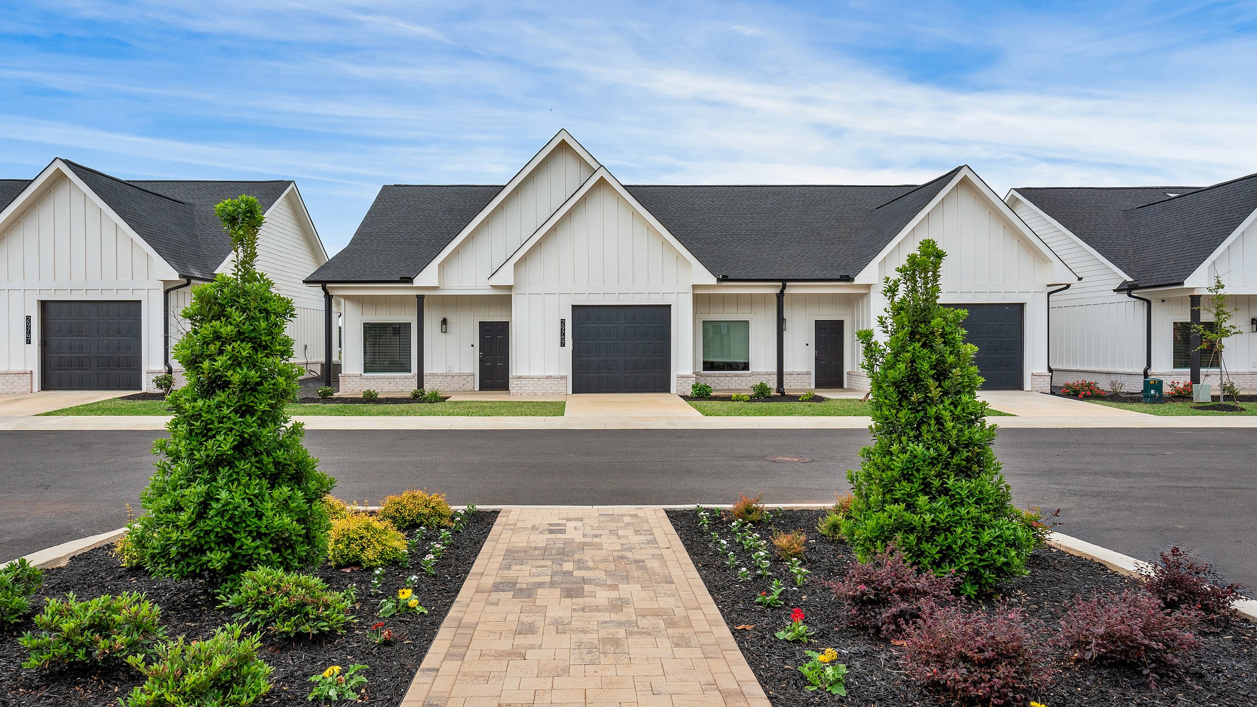 Charming row of modern townhouses with elegant white facades, manicured gardens, and a clear blue sky above.