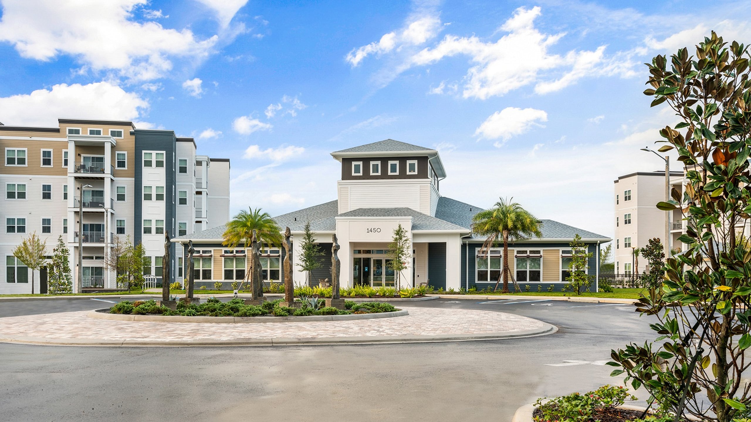 Elegant apartment complex with modern architecture, surrounded by lush landscaping and vibrant palm trees under a clear blue sky.