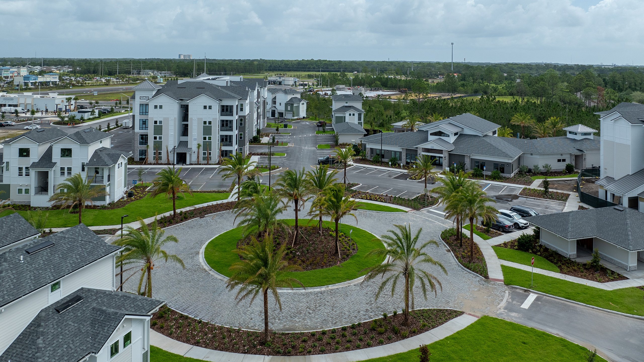 Beautiful aerial view of a modern apartment complex with lush green landscaping, palm trees, and spacious parking area on a sunny day.