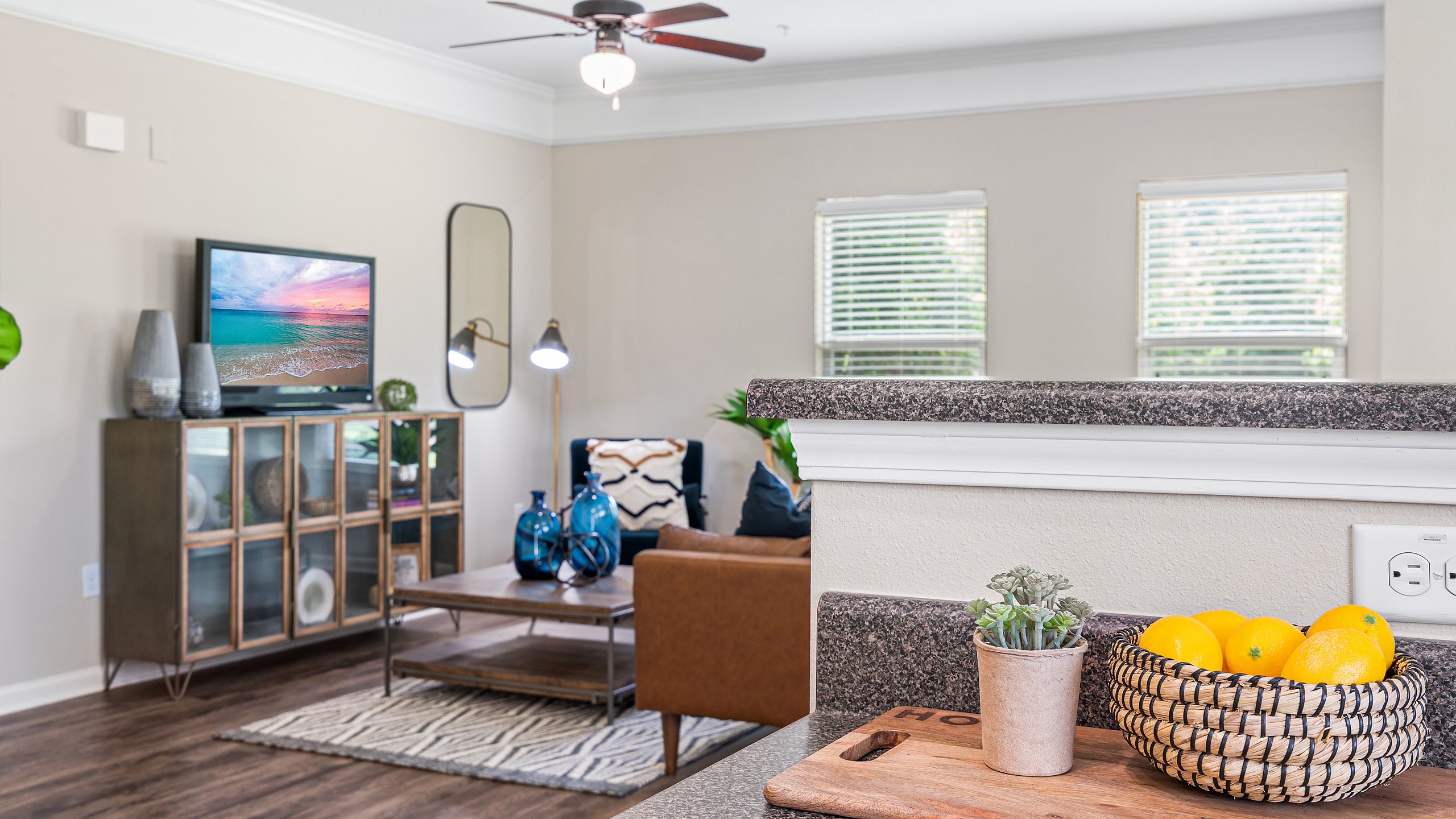 Inviting living room with modern decor, featuring a cozy armchair, vibrant blue vases, and a wall-mounted TV beneath a ceiling fan.