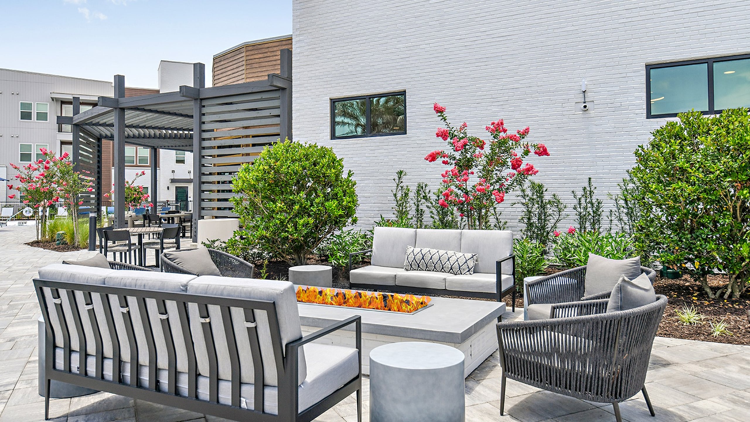 Chic outdoor patio with modern gray seating, vibrant greenery, and a sleek fire feature, perfect for relaxing and entertaining.