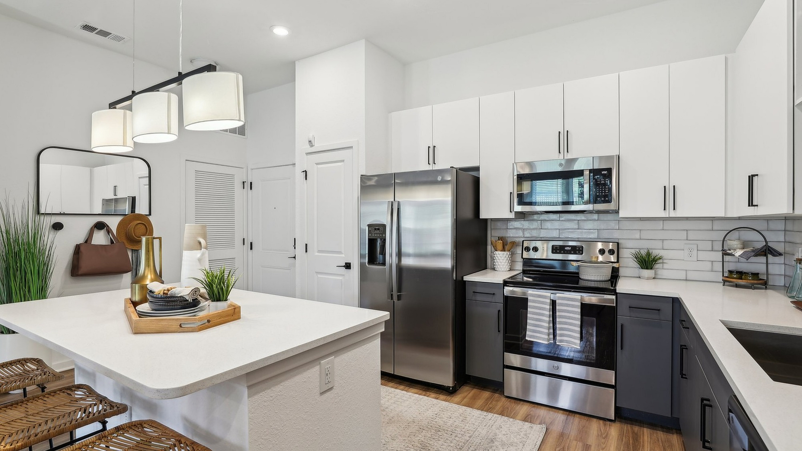 Modern kitchen with sleek stainless steel appliances, elegant two-tone cabinetry, and stylish pendant lighting. Cozy breakfast bar with woven chairs adds an inviting touch.