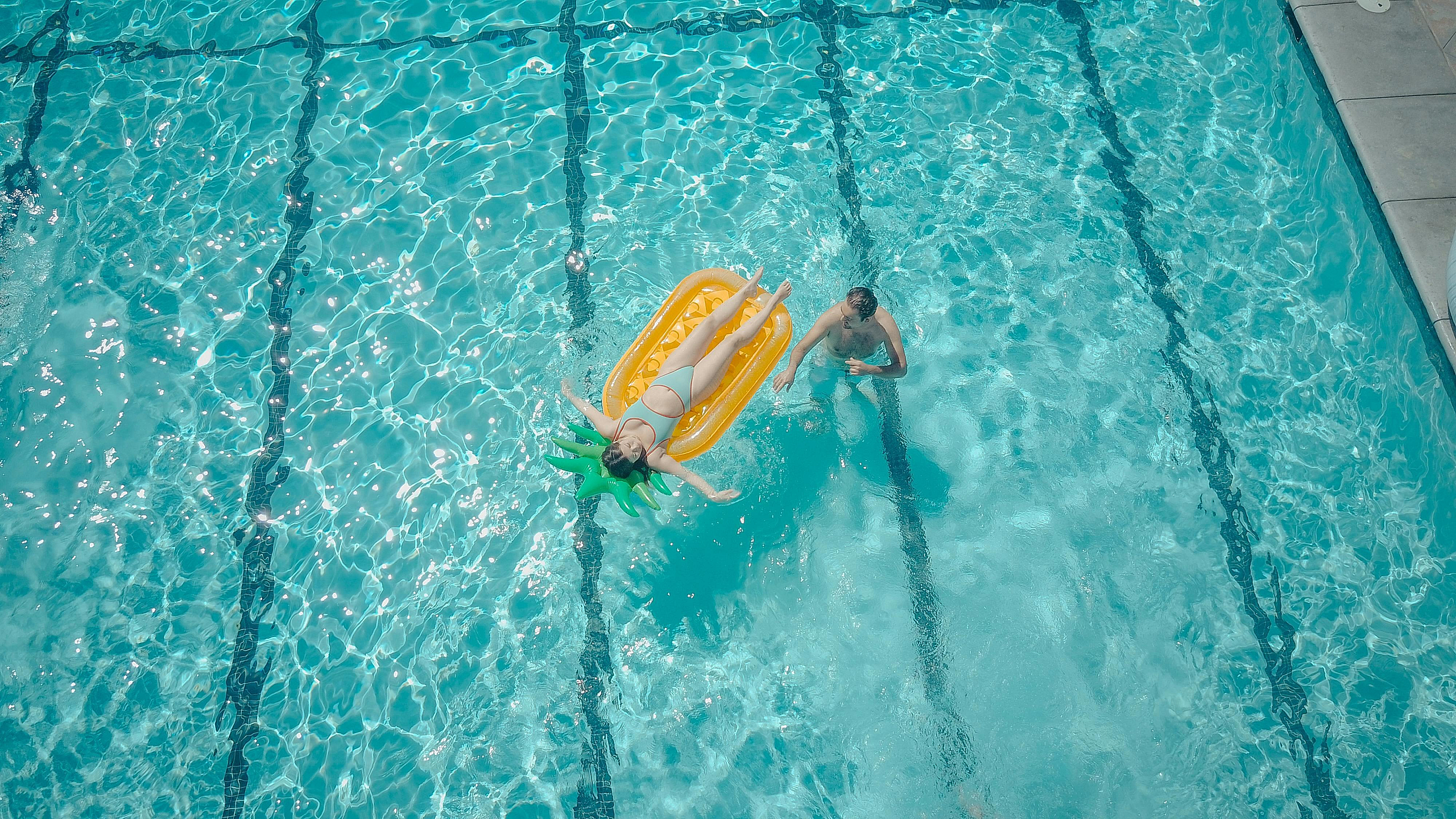 Inviting swimming pool with a relaxing atmosphere, featuring a person lounging on a vibrant float and another enjoying the crystal-clear water.