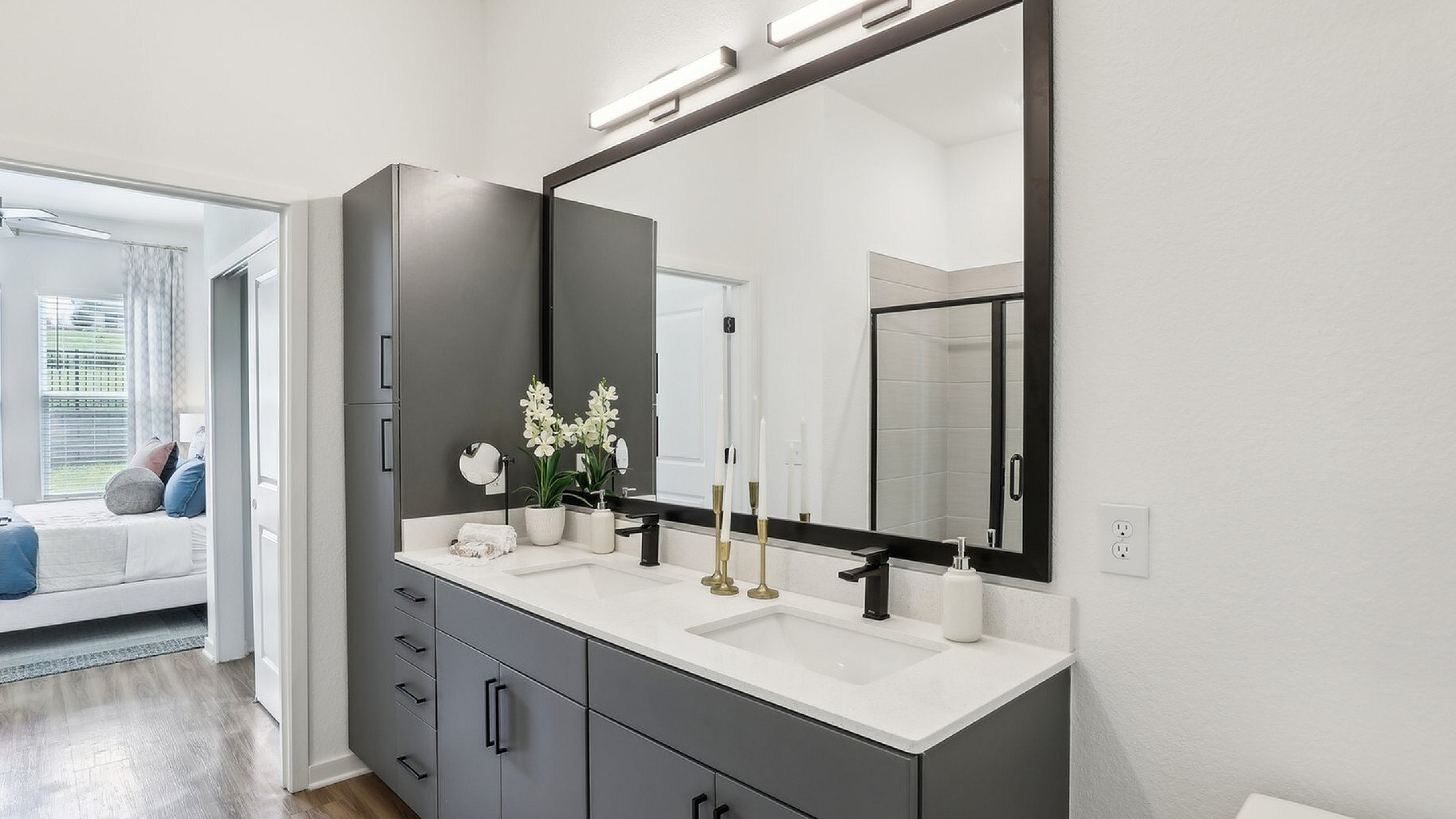 Elegant bathroom featuring a sophisticated double vanity, large mirror, and sleek cabinetry, with a glimpse into a cozy bedroom with natural light.
