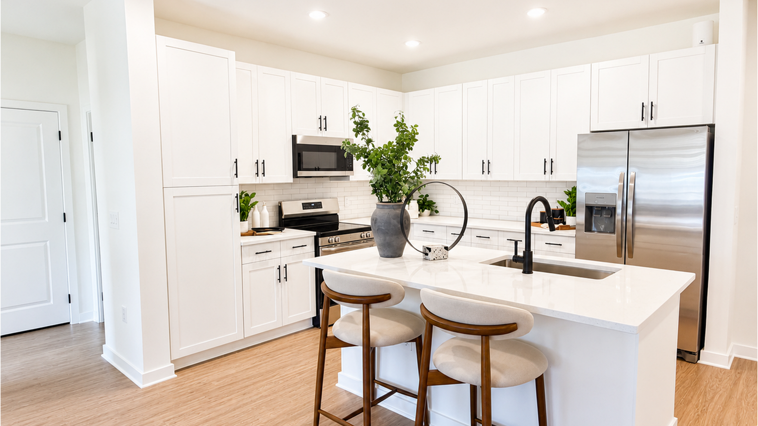 Modern kitchen featuring sleek white cabinetry, stainless steel appliances, and a chic breakfast bar with elegant seating.