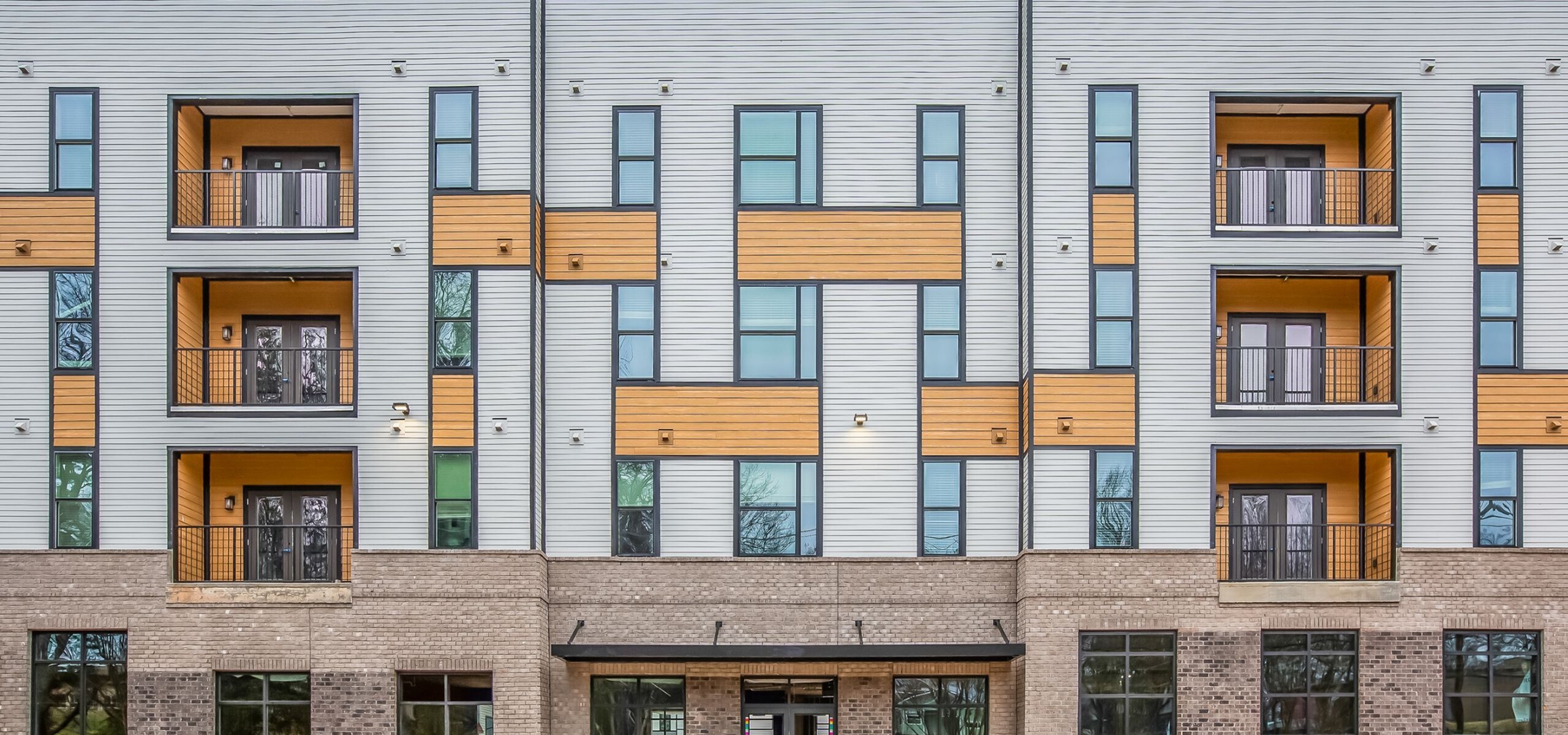 Modern apartment building with stylish balconies, sleek design elements, and a mix of brick and paneling for an attractive urban appeal.