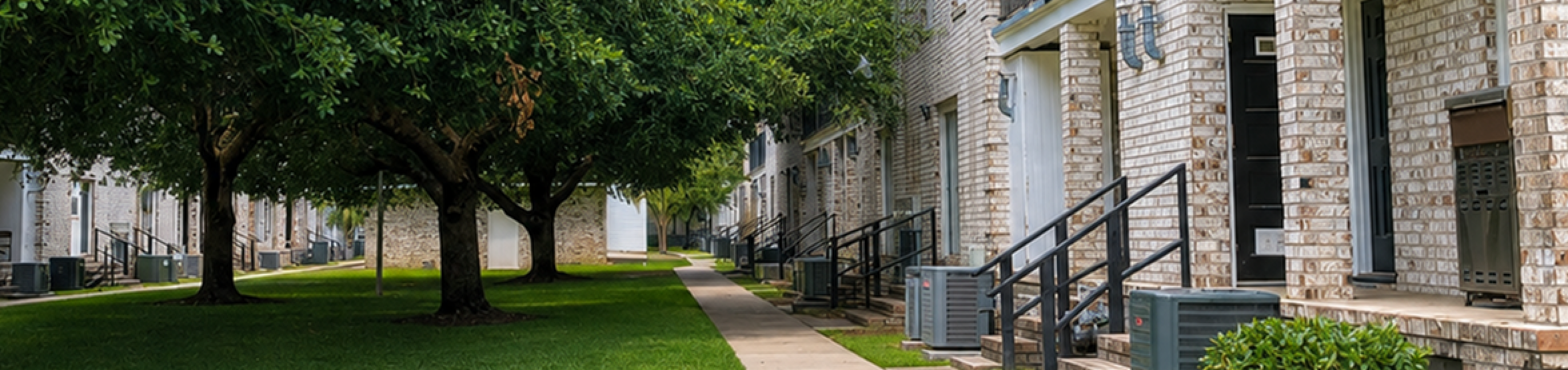 Idyllic apartment complex with brick exterior, lush green lawns, and inviting walkways under blue skies.