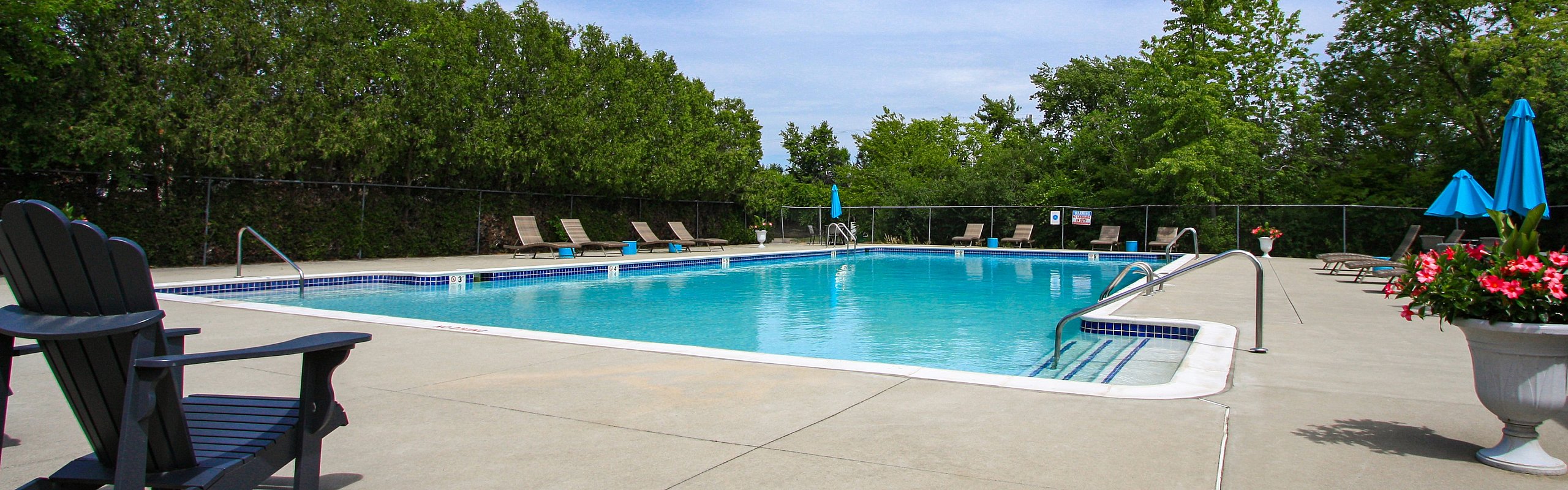 Inviting outdoor pool area with lush greenery, lounge chairs, and vibrant blue umbrellas under a clear sky.