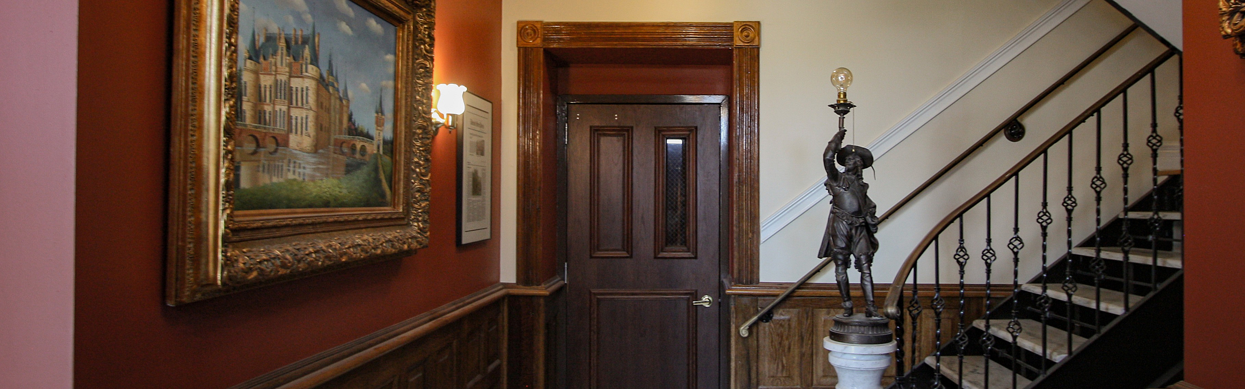 Elegant hallway with rich wood paneling, sophisticated artwork, and intricate staircase design.
