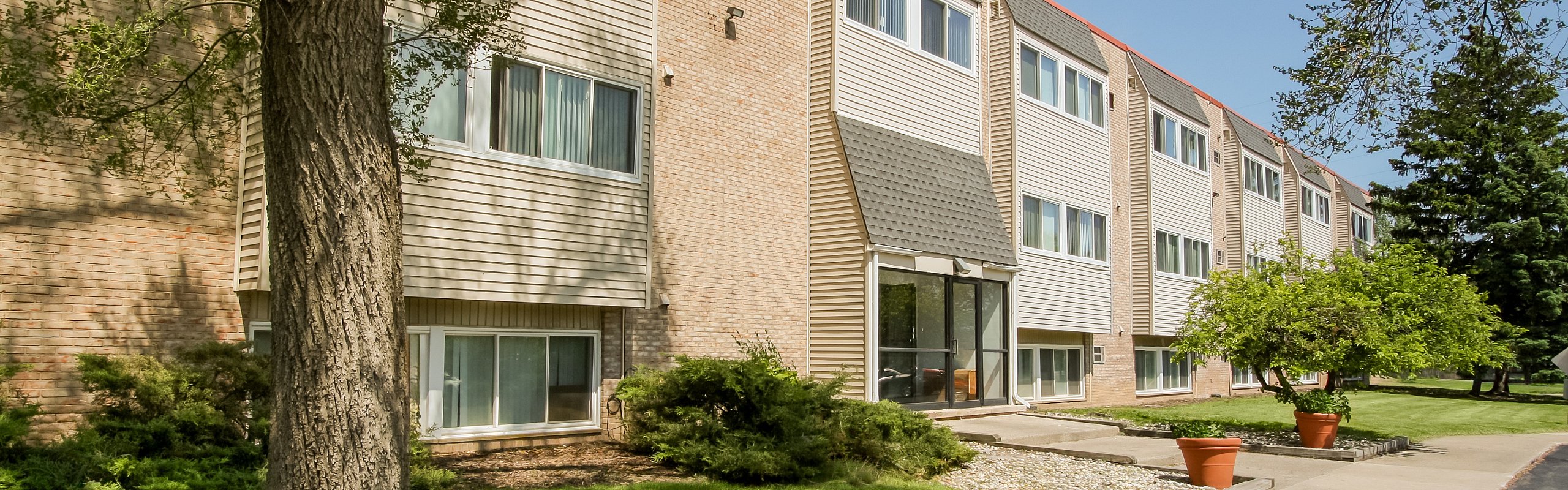 Charming apartment exterior with lush green lawns, mature trees, and a welcoming entrance, ideal for serene living.