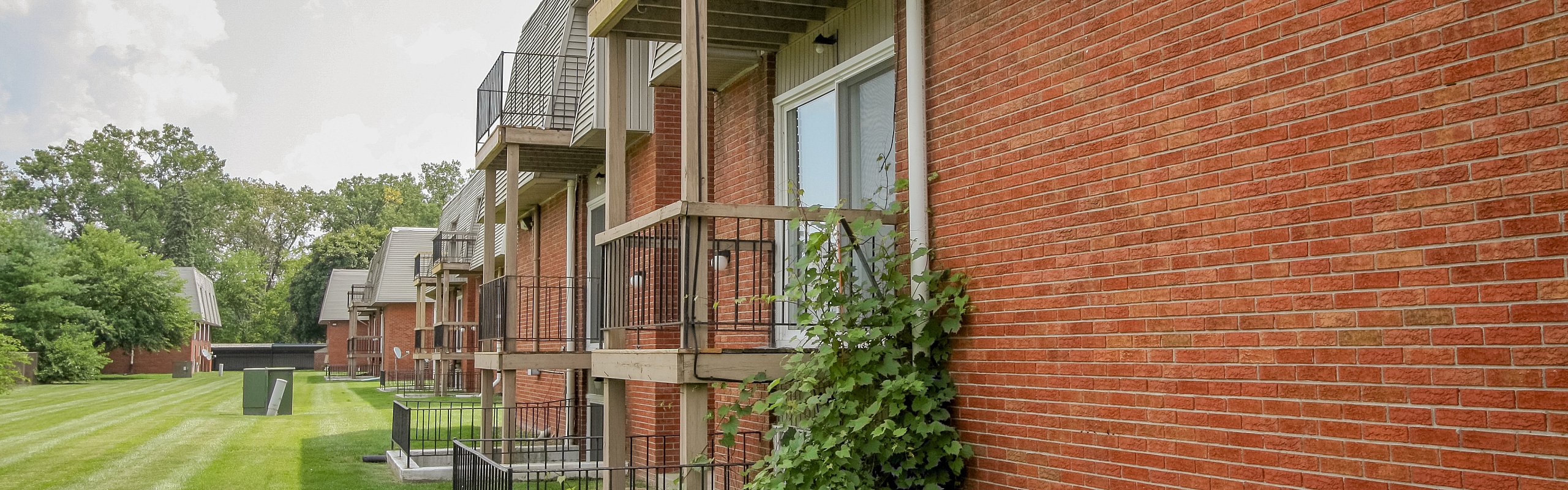 Charming brick apartment exterior with private balconies overlooking lush green lawns and serene surroundings.