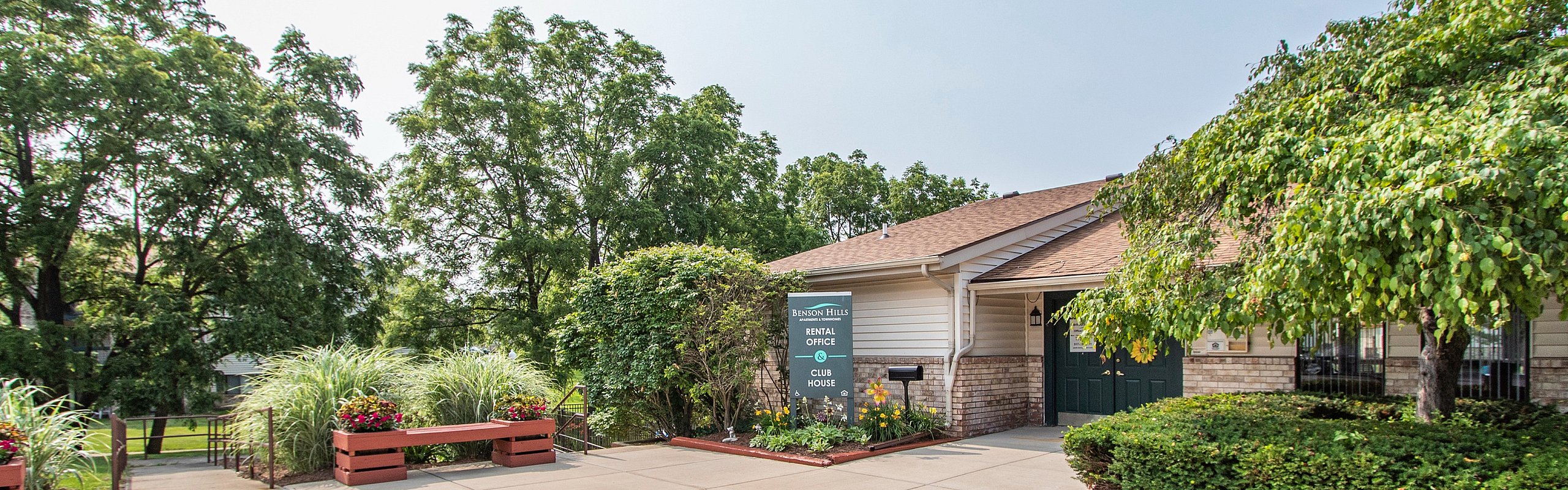 Inviting rental office entrance surrounded by lush greenery and well-maintained landscaping at Henson Hills.