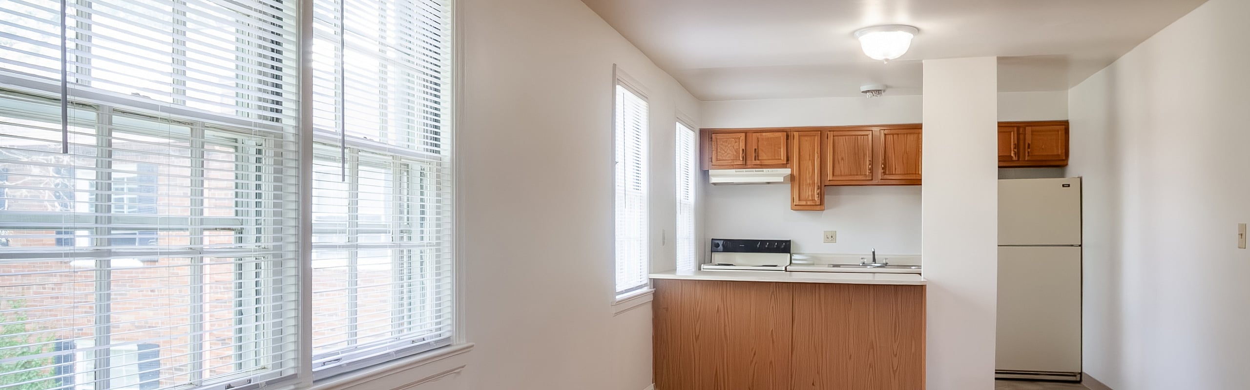 Bright kitchen area with large windows, white appliances, and wooden cabinetry, offering a cozy and inviting atmosphere.