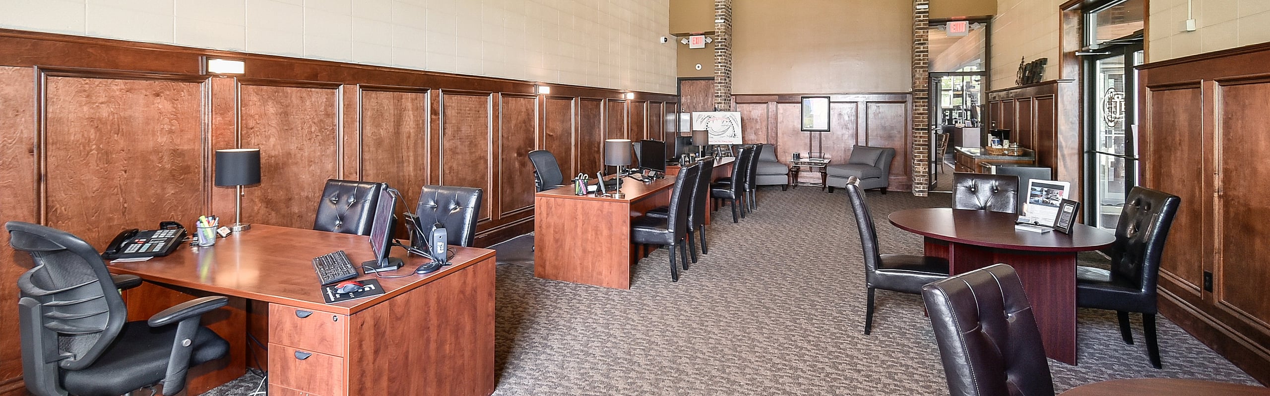 Elegant office space with rich wood paneling, modern desks, and plush black chairs, perfect for a sophisticated work environment.