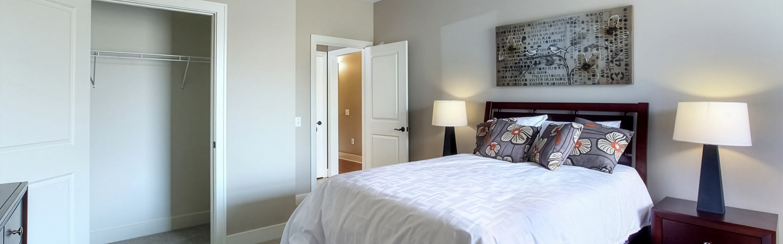 Cozy bedroom featuring elegant floral pillows, warm lighting, and spacious closet in modern apartment.