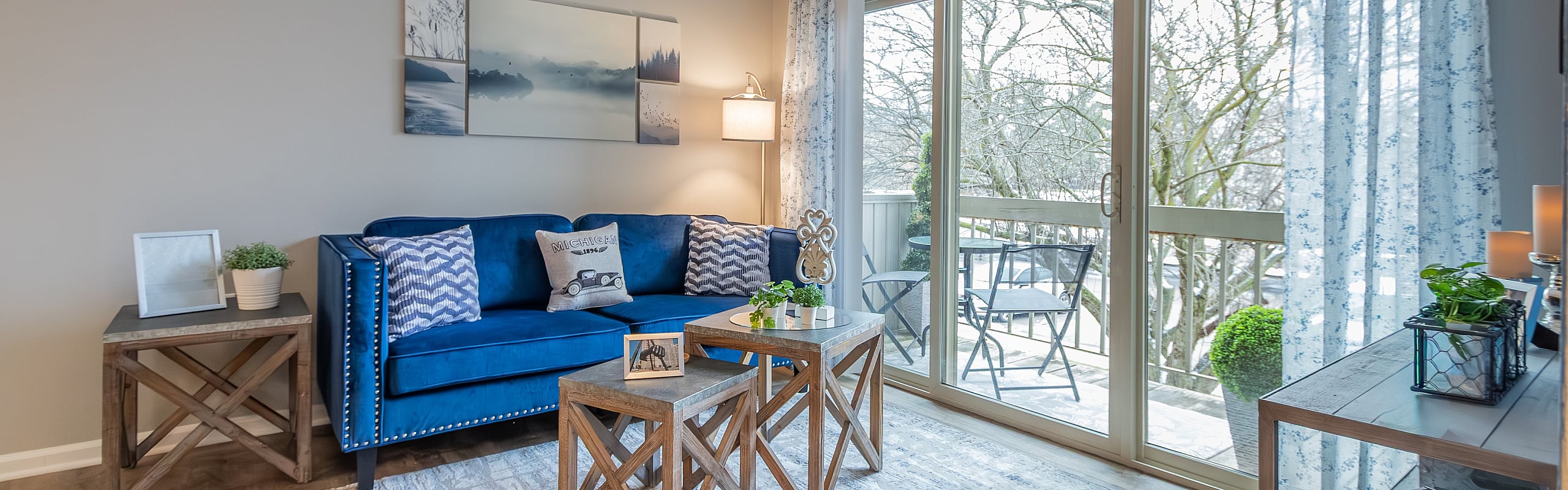 Inviting living room with a plush blue sofa, charming decor, and bright natural light through large glass doors leading to a cozy balcony.