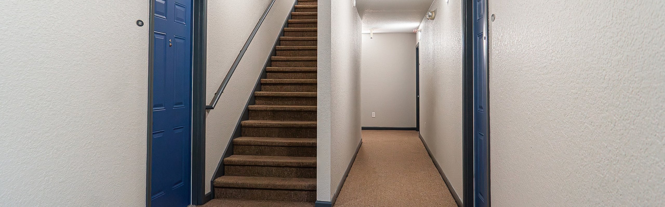 Inviting hallway with blue doors and carpeted staircase, offering a glimpse into a welcoming apartment complex.