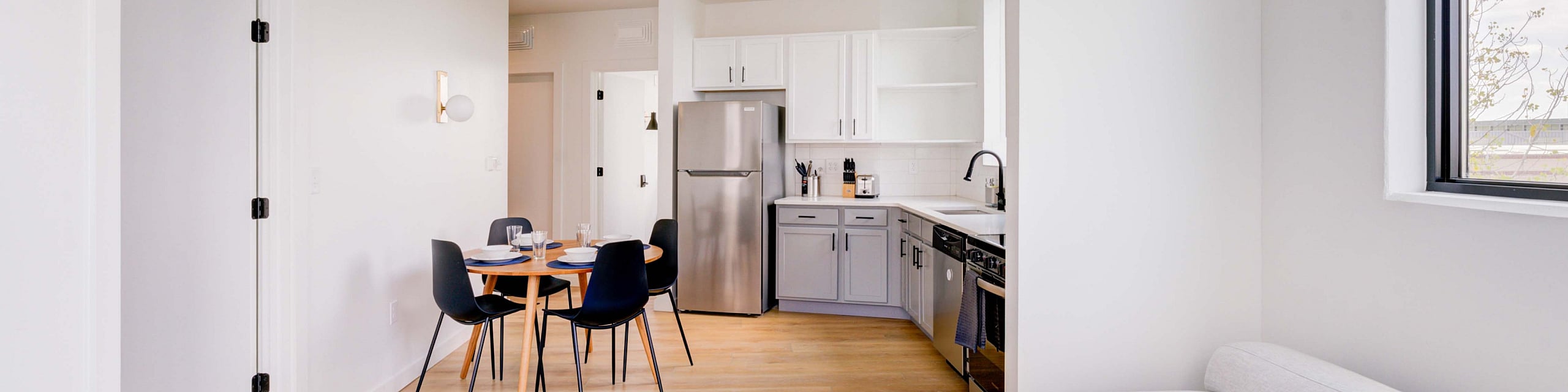 Bright and modern living space featuring a cozy L-shaped sofa, chic dining area, and a stylish kitchen with stainless steel appliances.